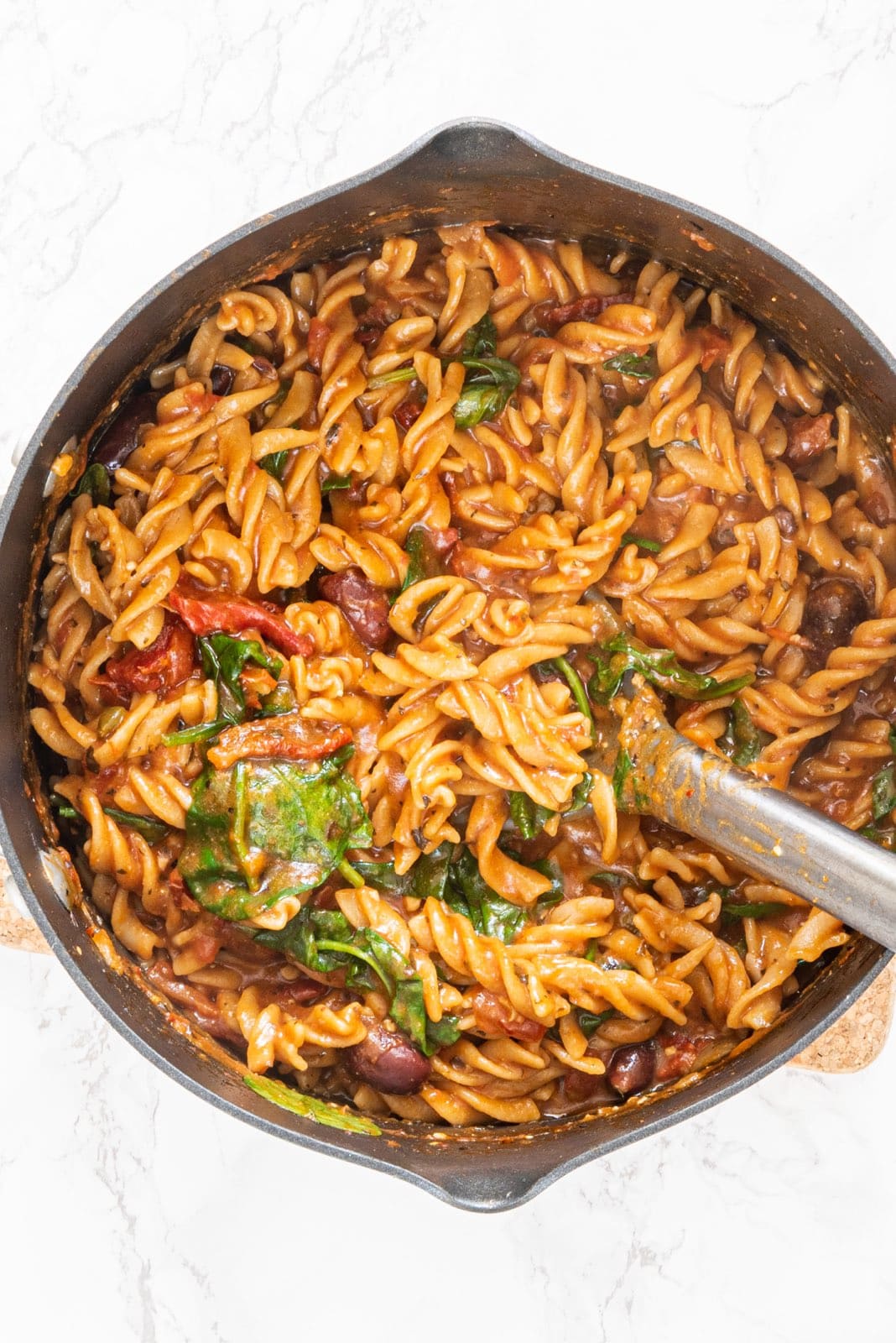 A large pot of pasta and a silver metal spoon in it.