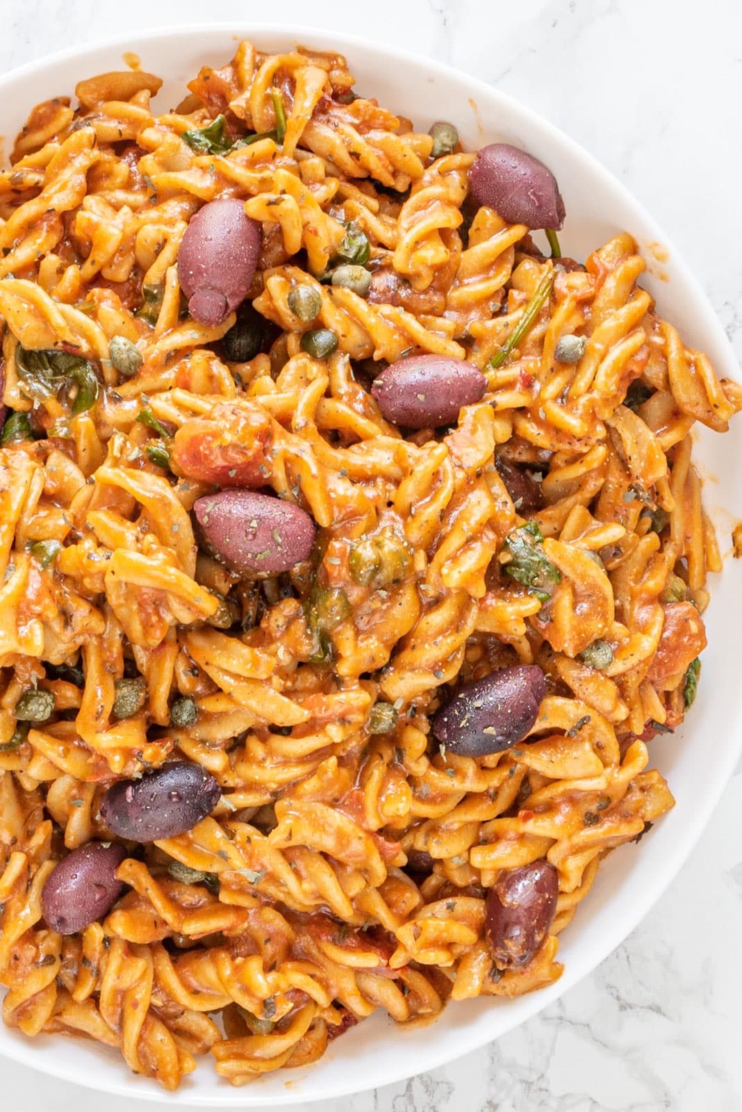 A large bowl of vegan italian pasta topped with kalamata olives.