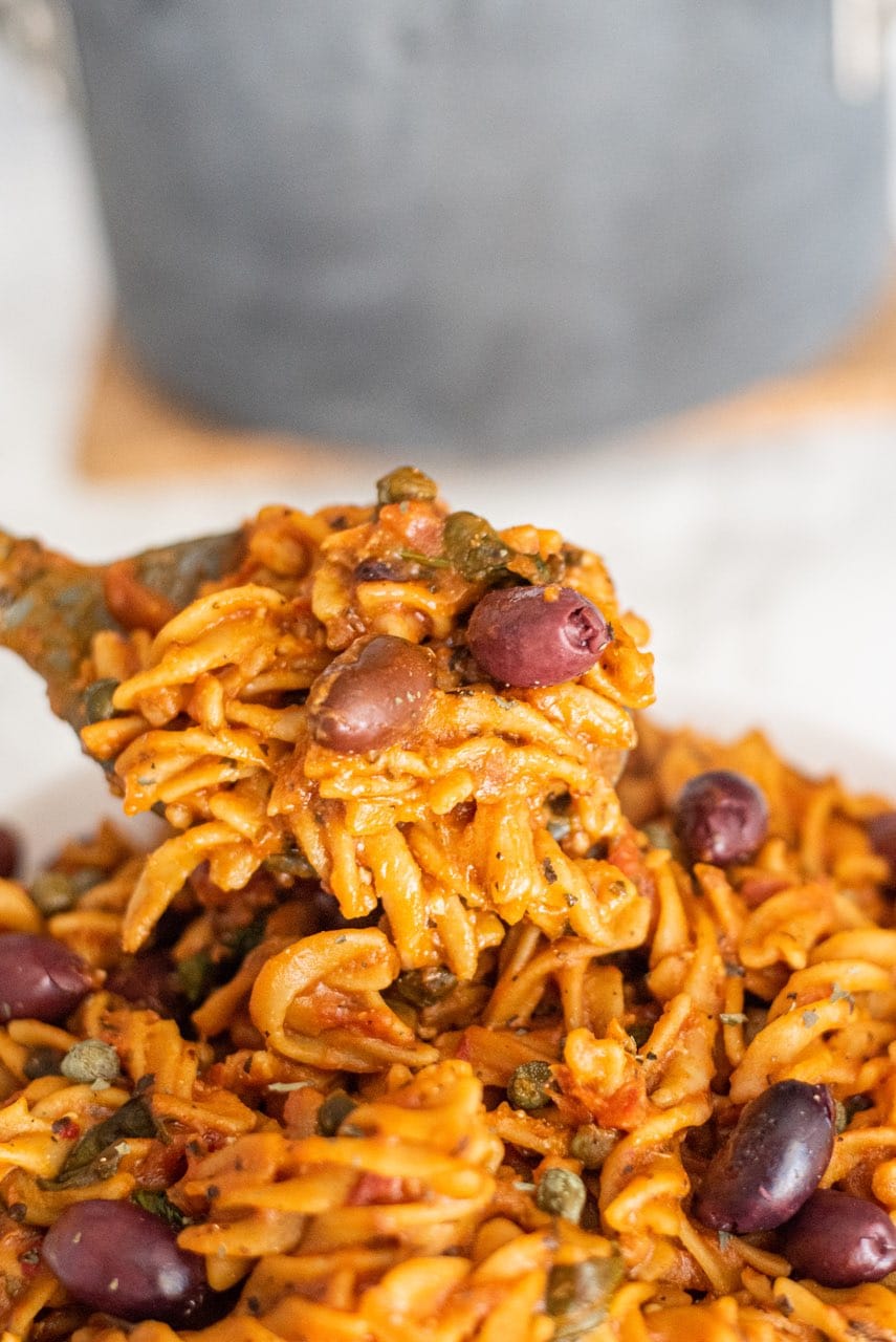 A bowl of pasta and a spoon holding a scoop of it.