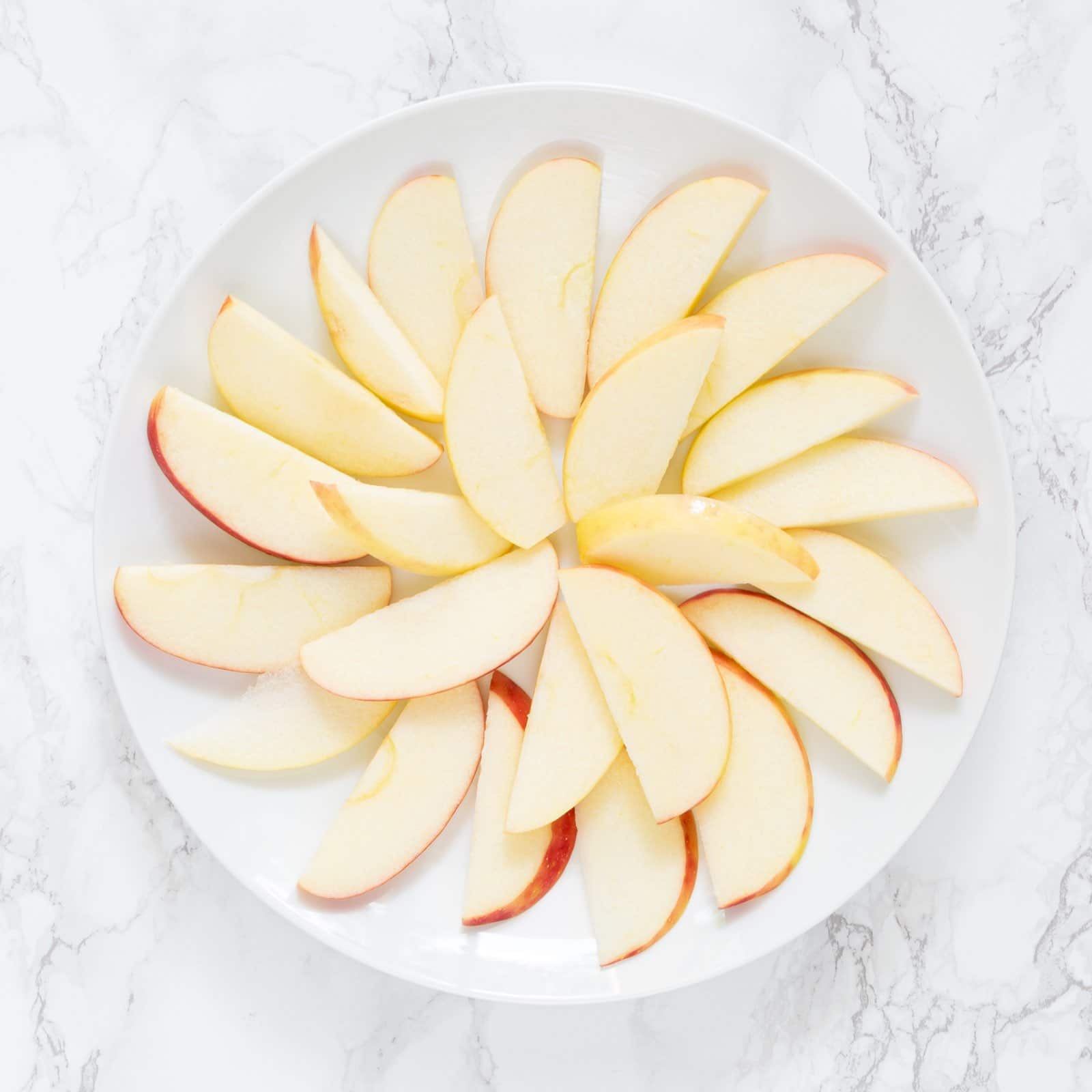 A white plate with apple slices arranged in a flat layer on it.