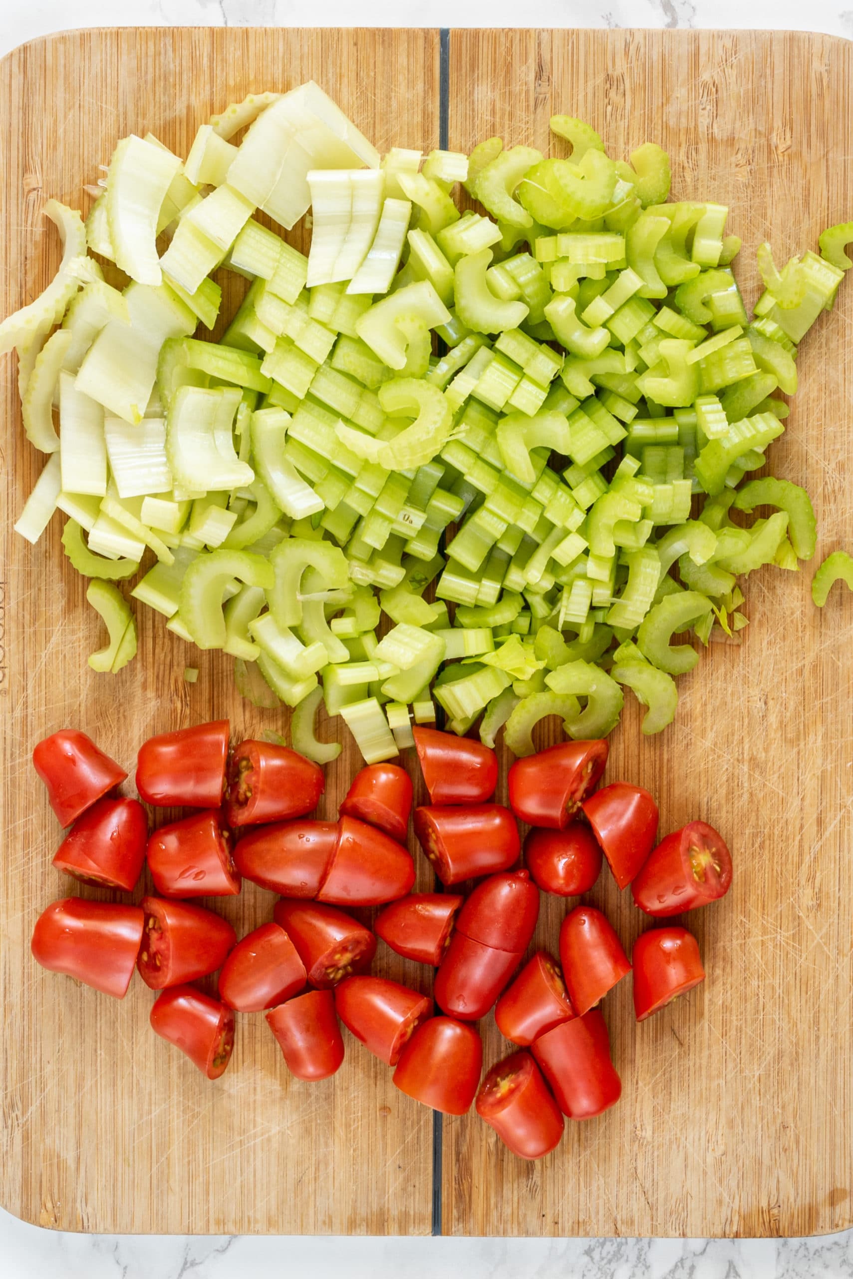 A wood cutting board filled with chopped tomatoes on one half and chopped celery on the other half.