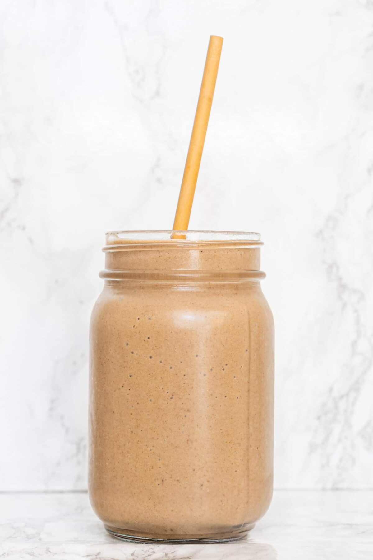 Cinnamon Bun Cauliflower Smoothie in a clear glass jar with a straw sticking out from the top.