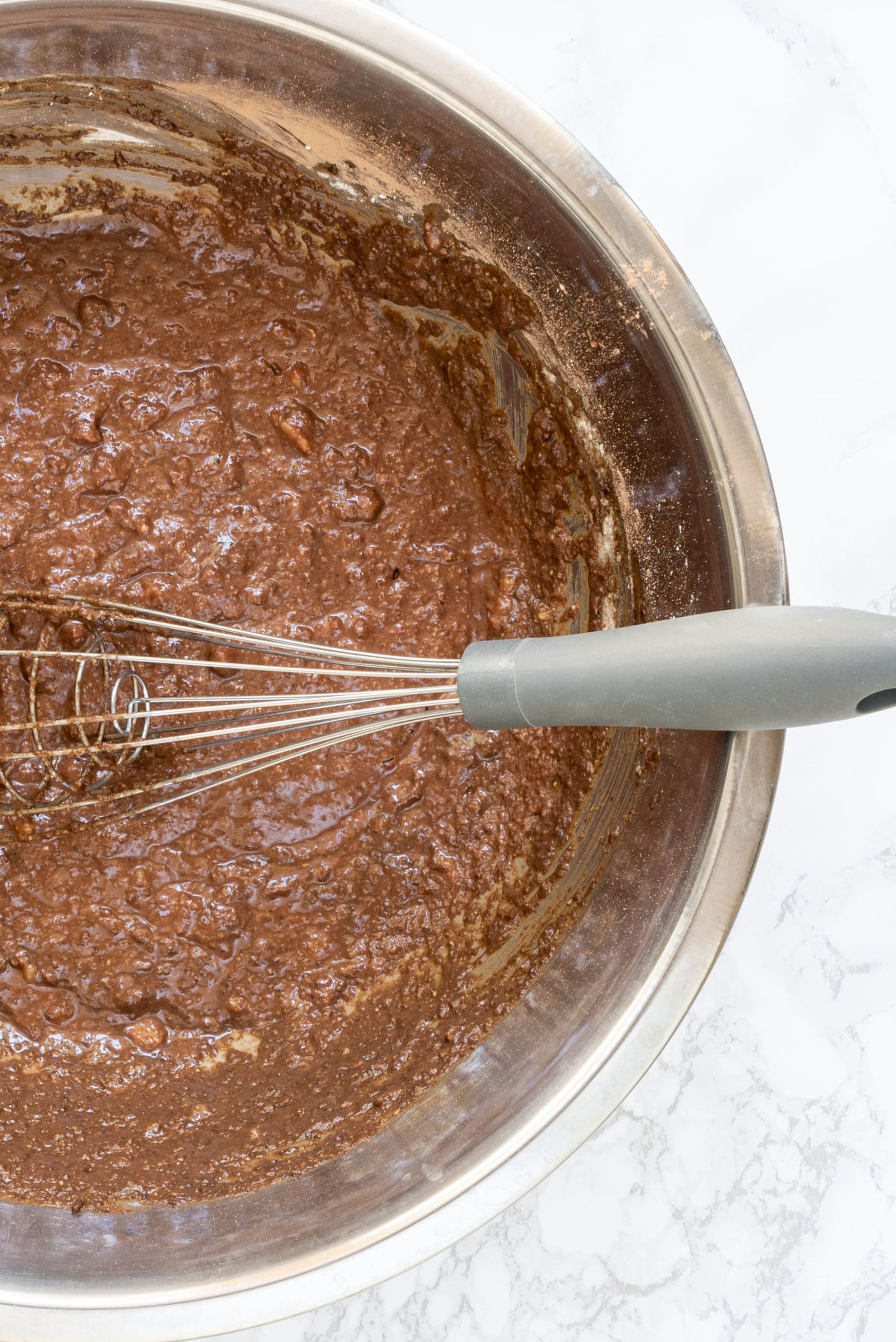 A silver bowl with vegan brownie banana bread batter in it and a whisk.