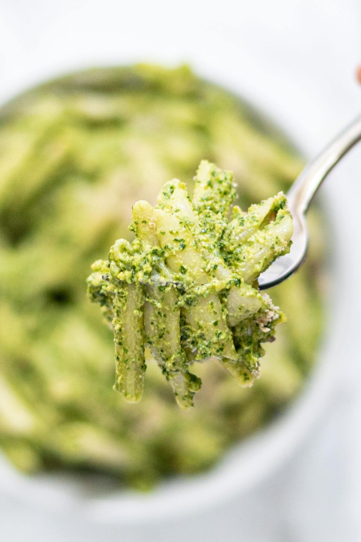 A silver fork with pieces of penne pesto pasta on it.