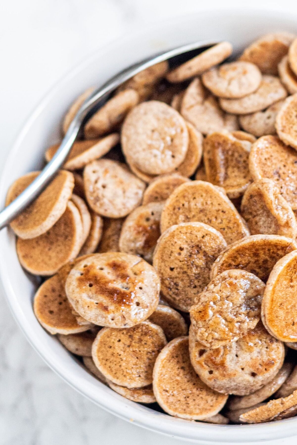 A white bowl of pancake cereal and a silver spoon in the bowl.