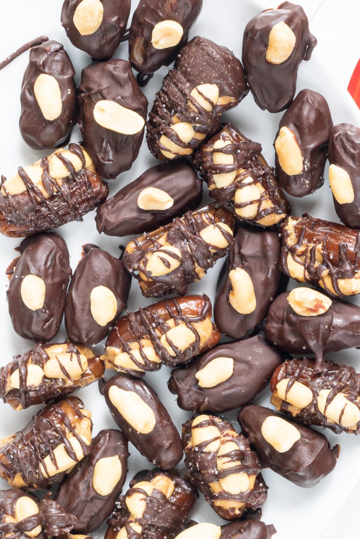 A plate of dates covered in chocolate topped with peanuts and salt.