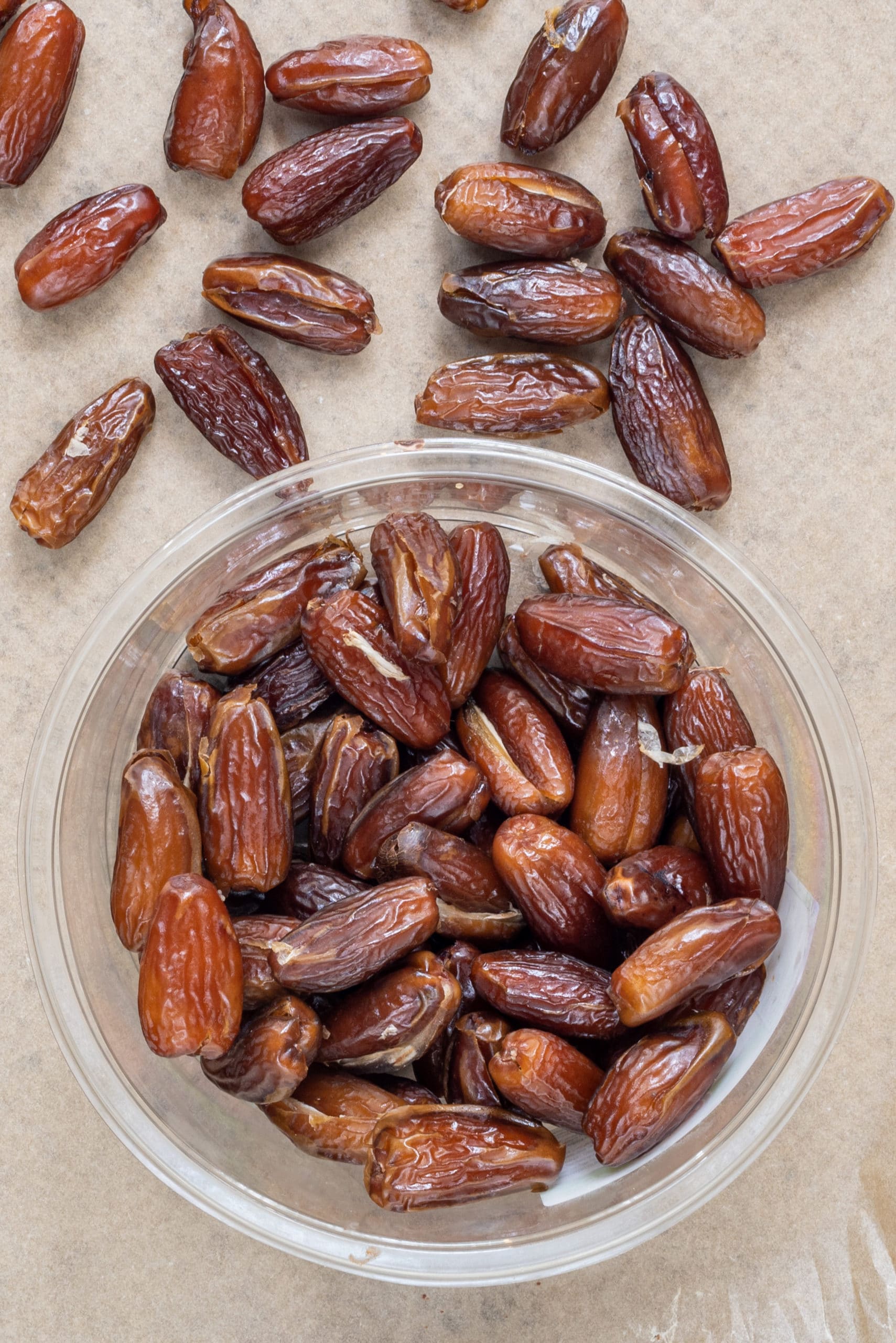 A baking sheet lined with parchment paper with a bowl of dates on it and dates on the pan.