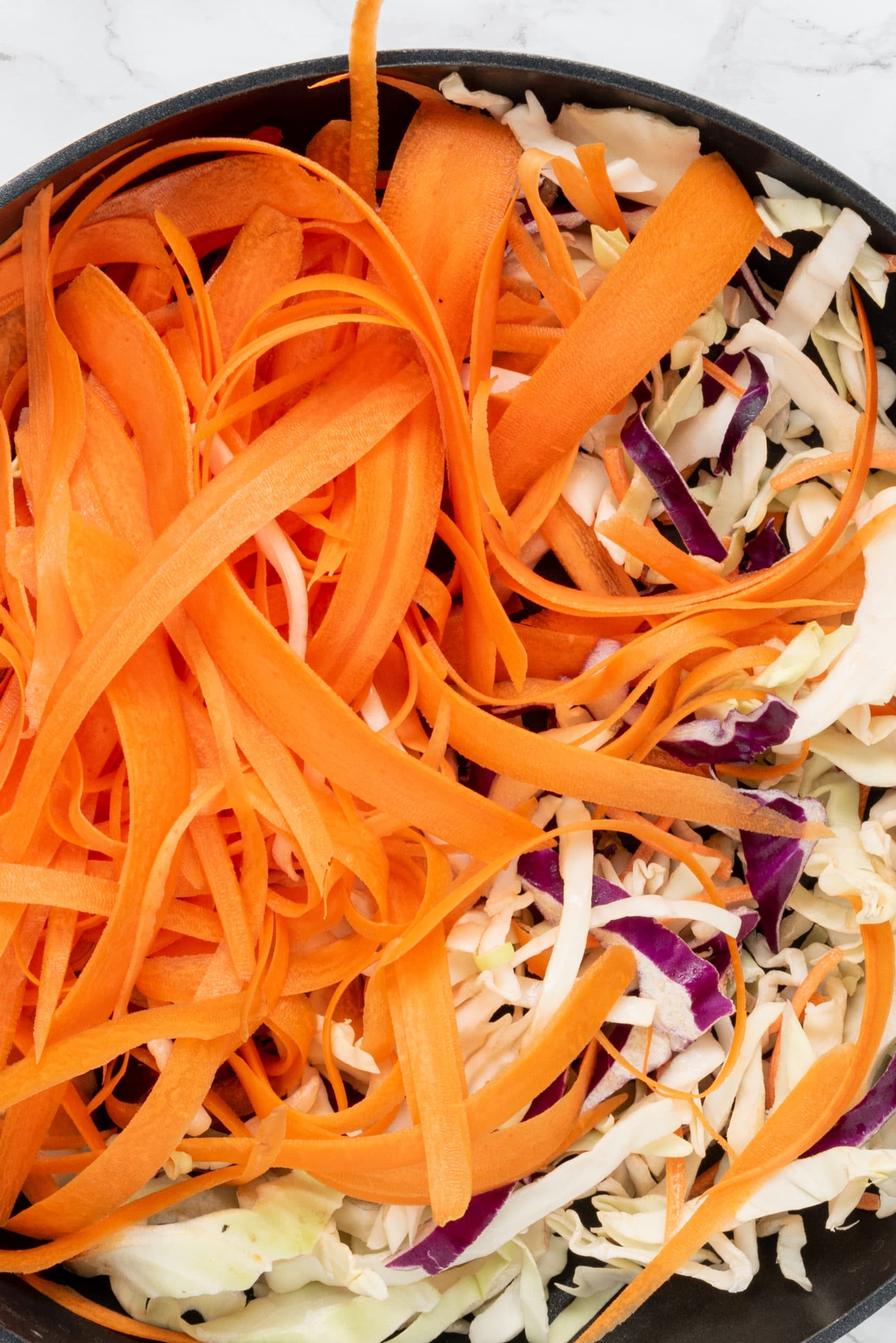 A black frying pan filled with shredded carrots and cabbage.