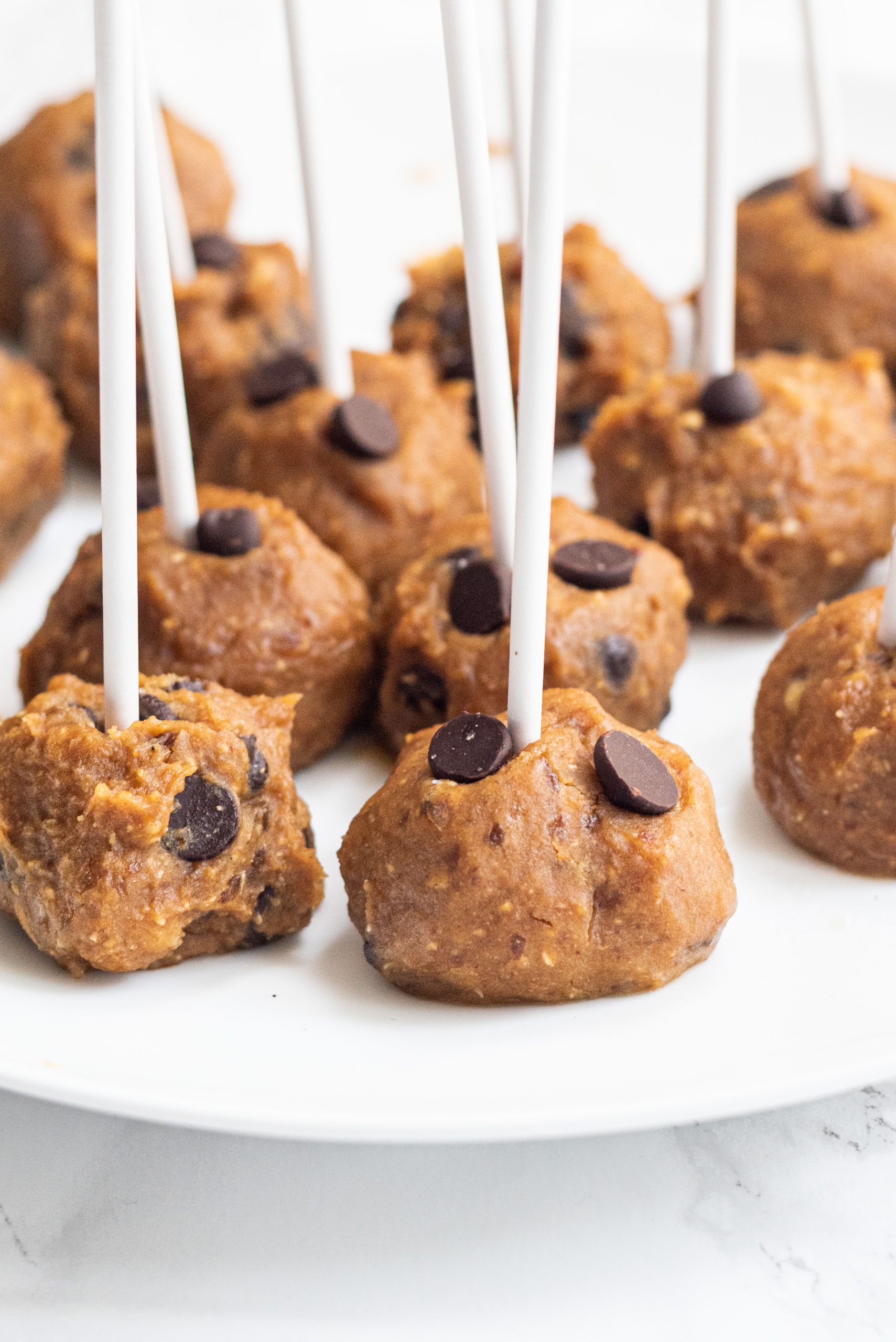 A plate of cookie dough balls on white sticks.