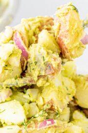 A white bowl filled with Healthy Vegan Potato Salad with a silver spoon sticking out of the bowl with potato salad on it.