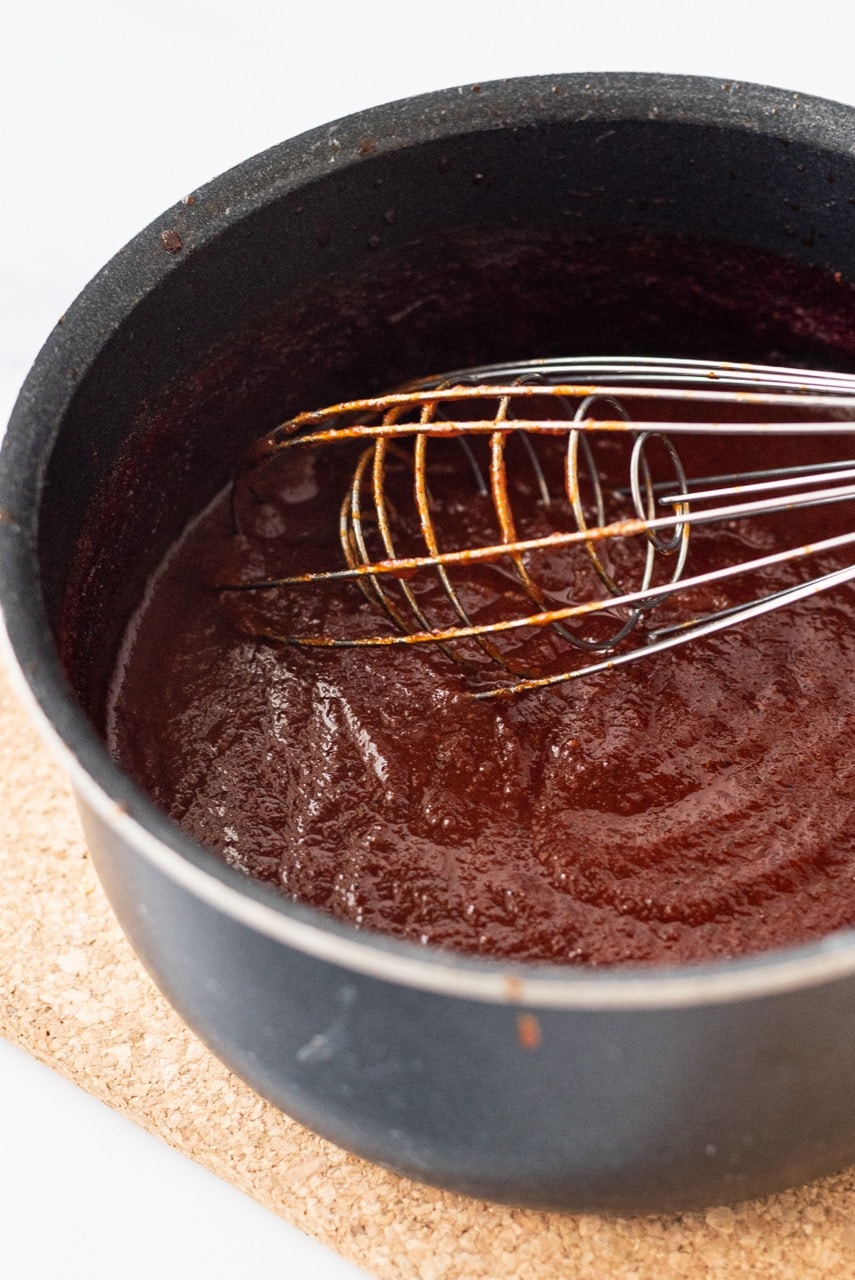A black sauce pan filled with barbecue sauce and a silver whisk.
