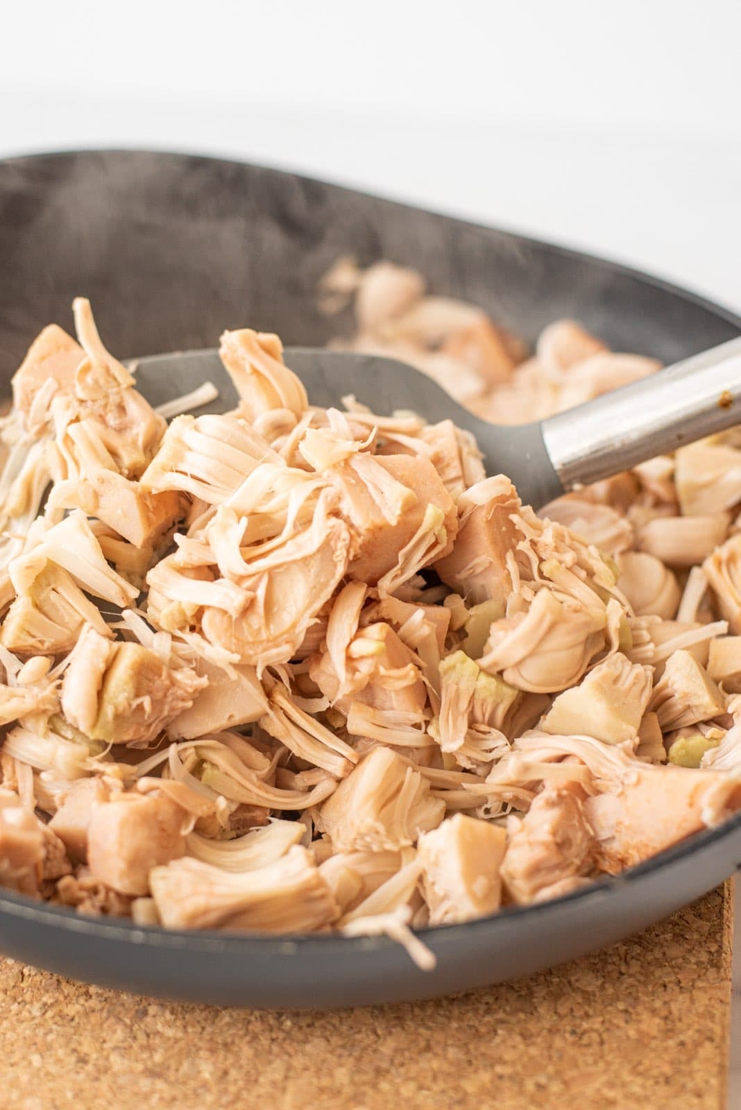 A pan filled with shredded jackfruit and a silicone grey spatula in it.