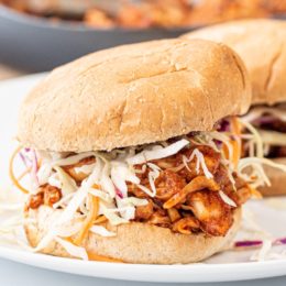 Two jackfruit sandwiches on burger buns on a white plate.