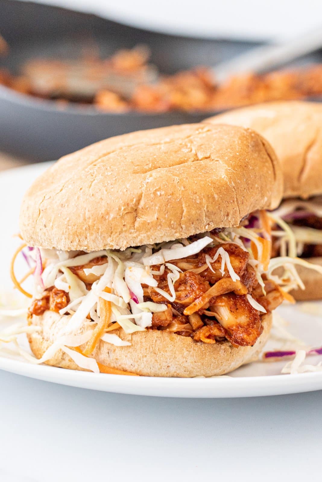Two jackfruit sandwiches on burger buns on a white plate.