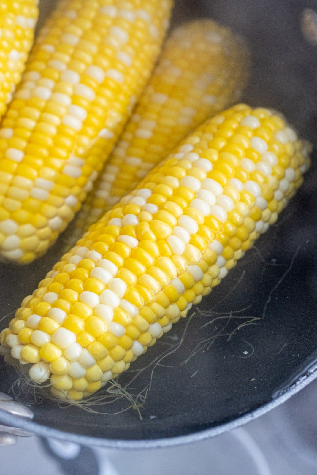 A large pot filled with water and 4 ears of fresh corn.