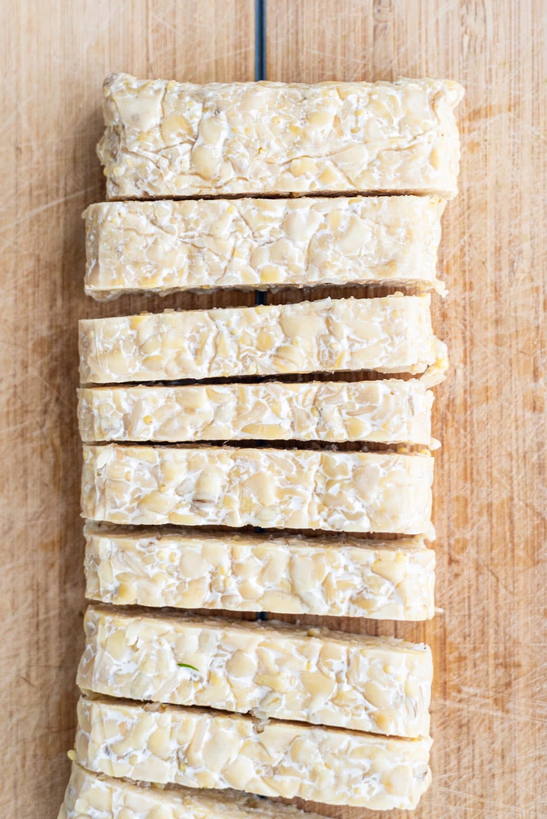 A wooden cutting board with strips of tempeh on it.