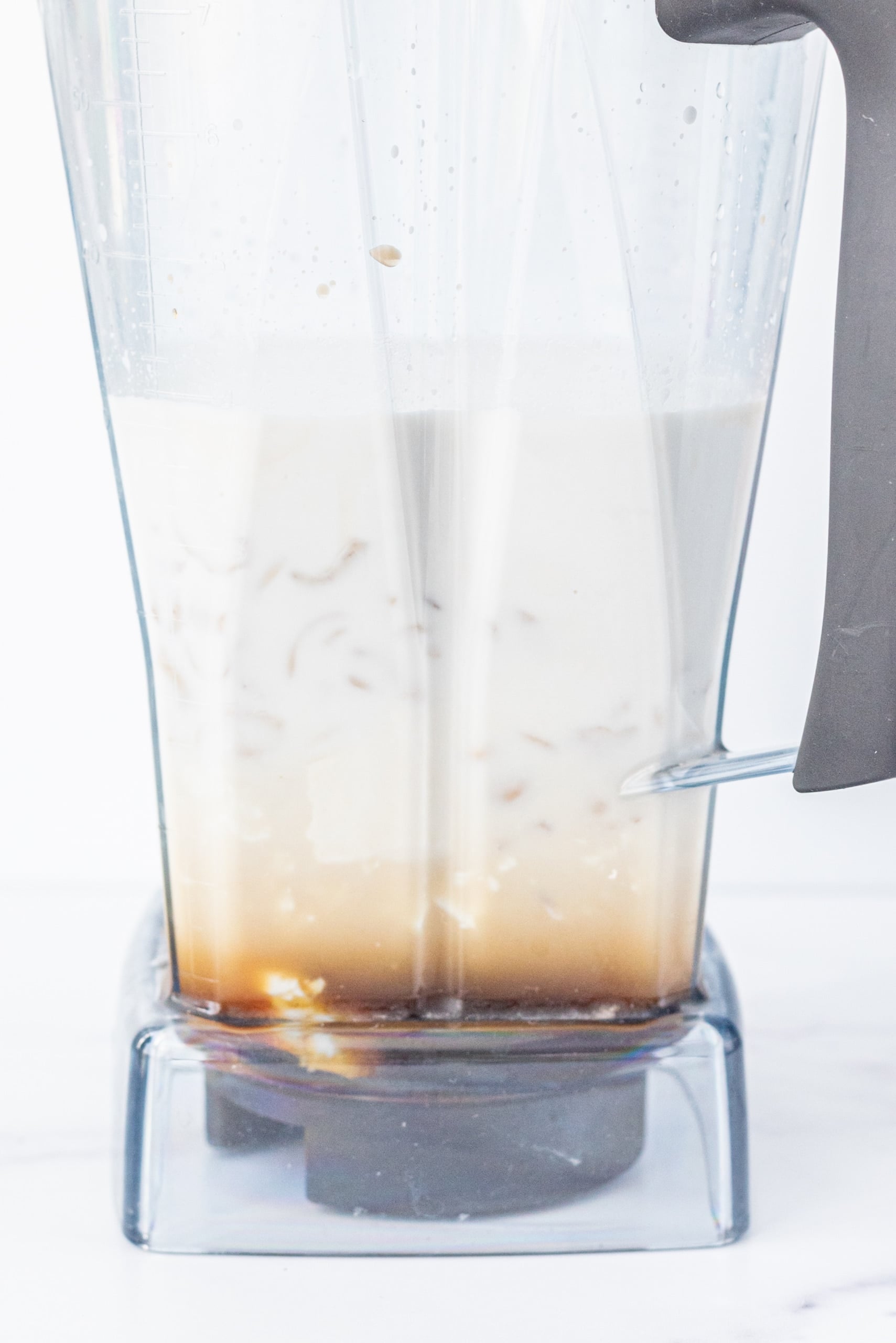 A blender filled with cashews, coconut milk, and maple syrup.