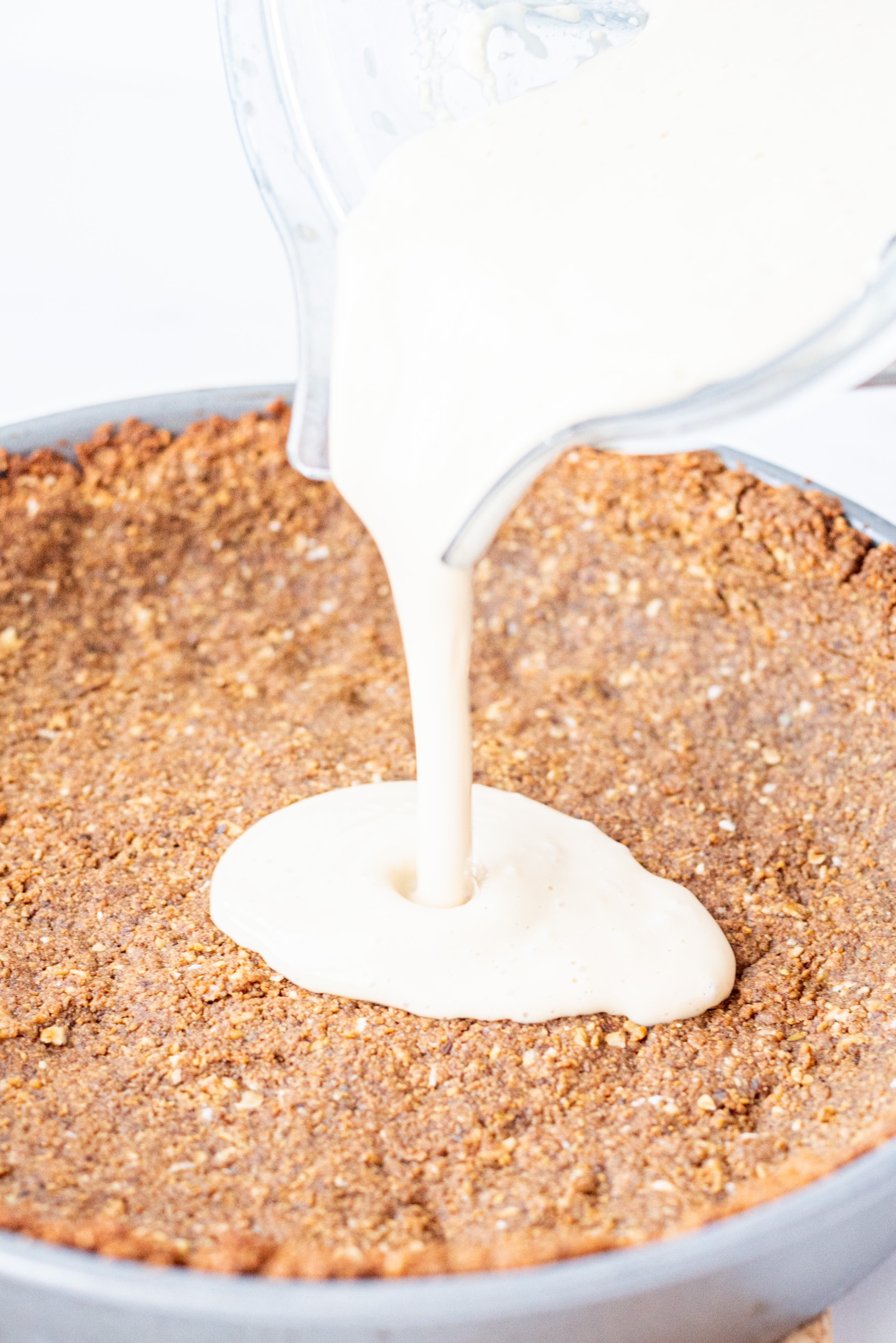 A pie crust and a blender pouring in a vanilla pie filling.