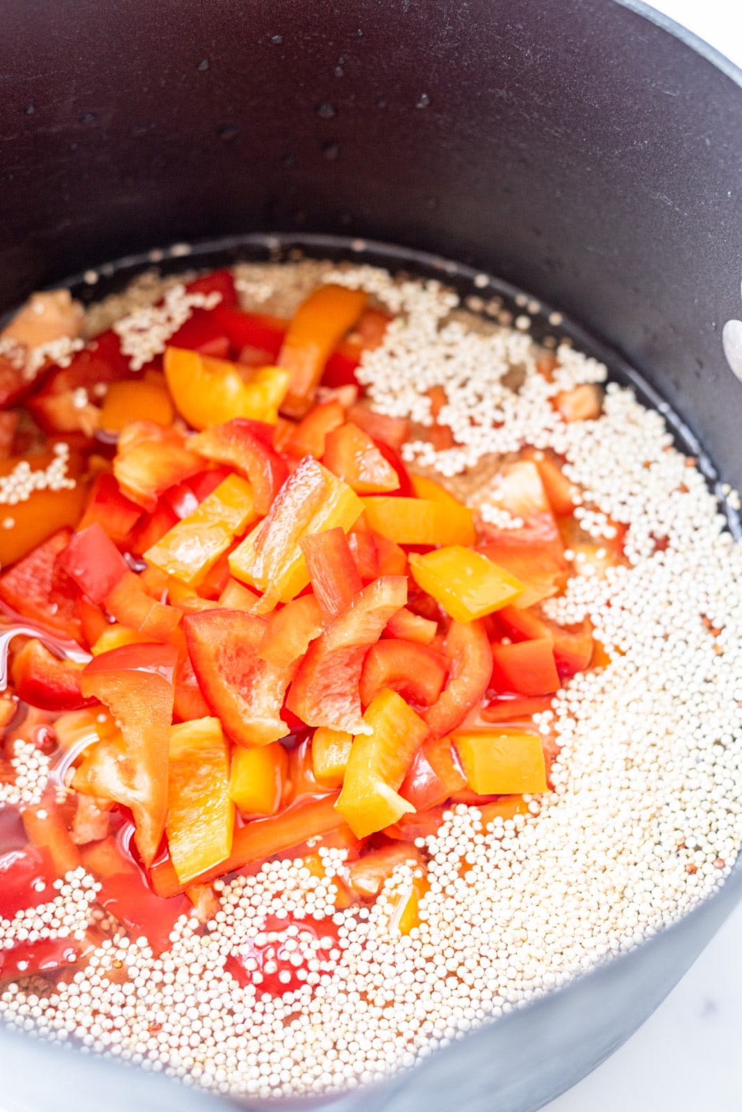 A black pot close-up filled with quinoa, water, and bell pepper.