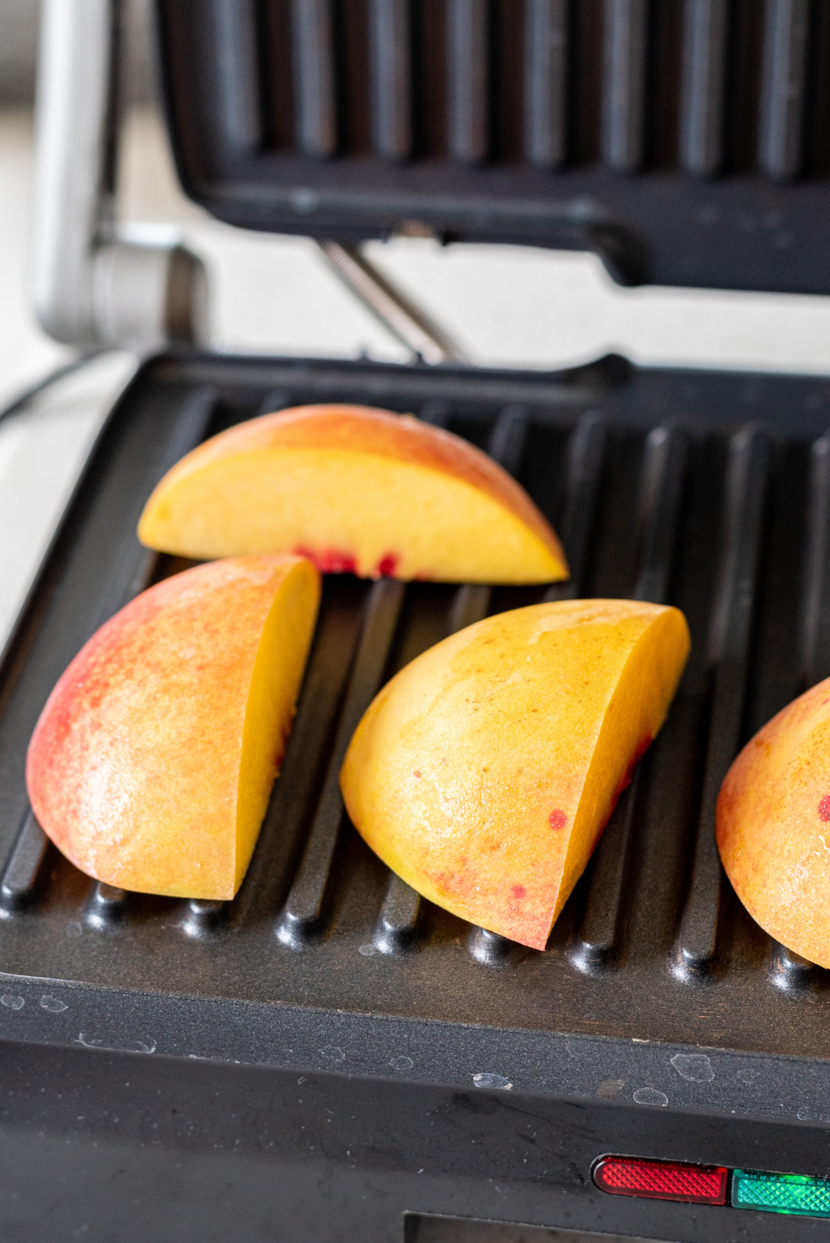 A black panini press with peach halves on it.