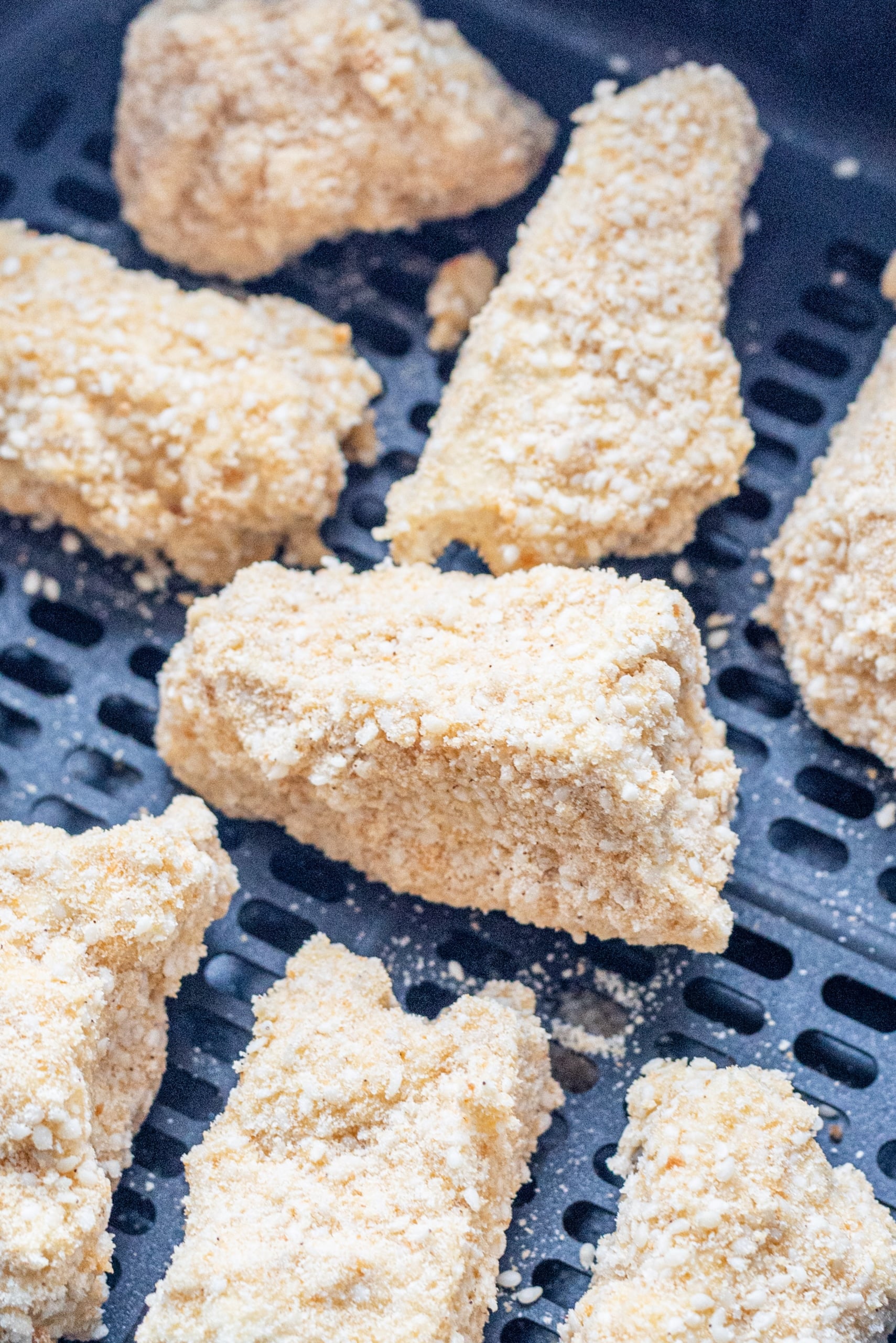 An air-fryer basket filled with uncooked tofu nuggets.