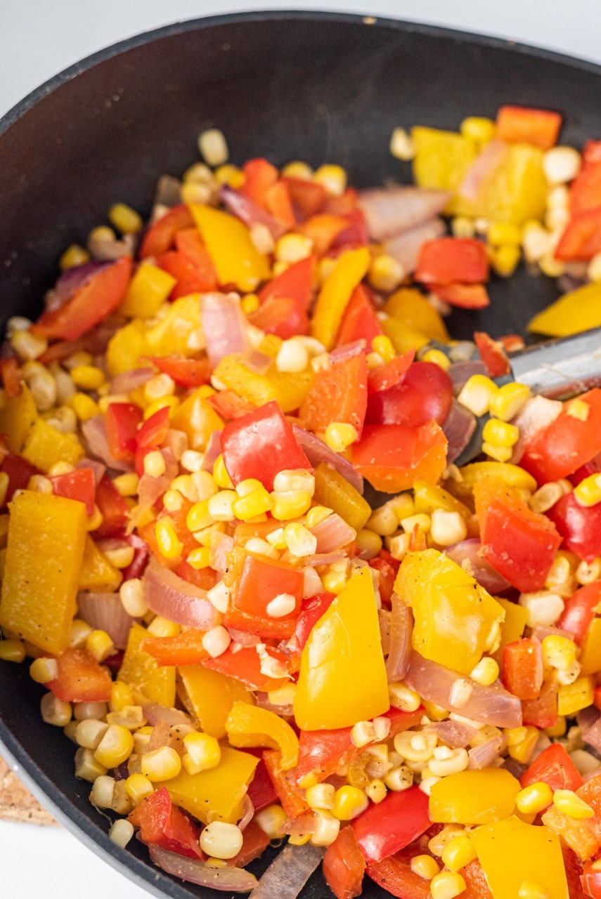 A black frying pan filled with chopped peppers, onions, and corn.