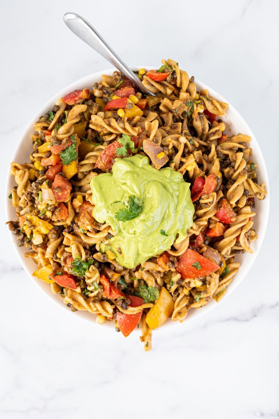 A white bowl of vegan taco pasta salad with a dollop of avocado lime cilantro sauce in the center.