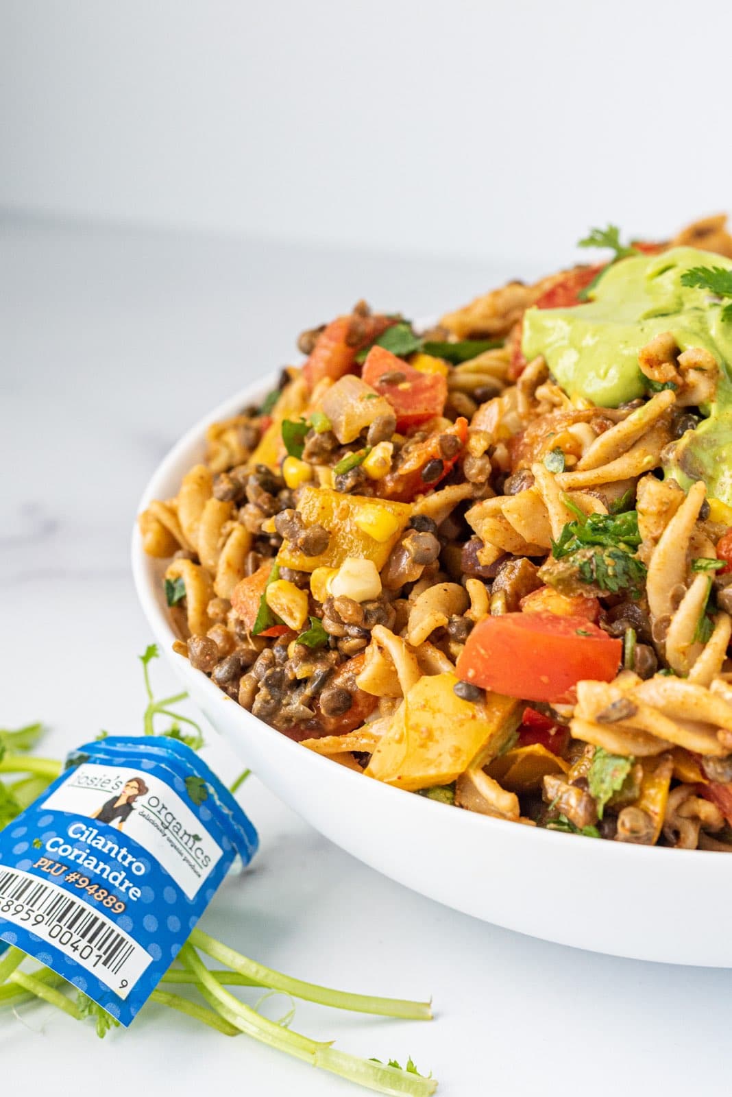 A white glass bowl with taco pasta salad in it and on the counter a bundle of fresh cilantro.