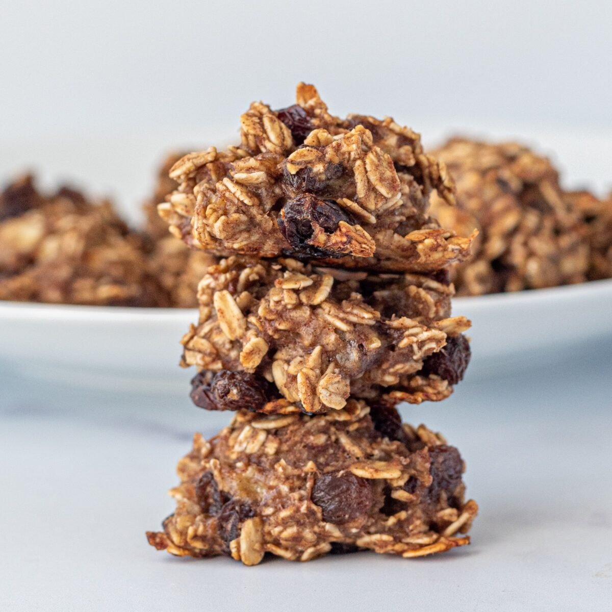 Three Oatmeal Banana Bites stacked on a white plate with another white plate in the background filled with the bites.