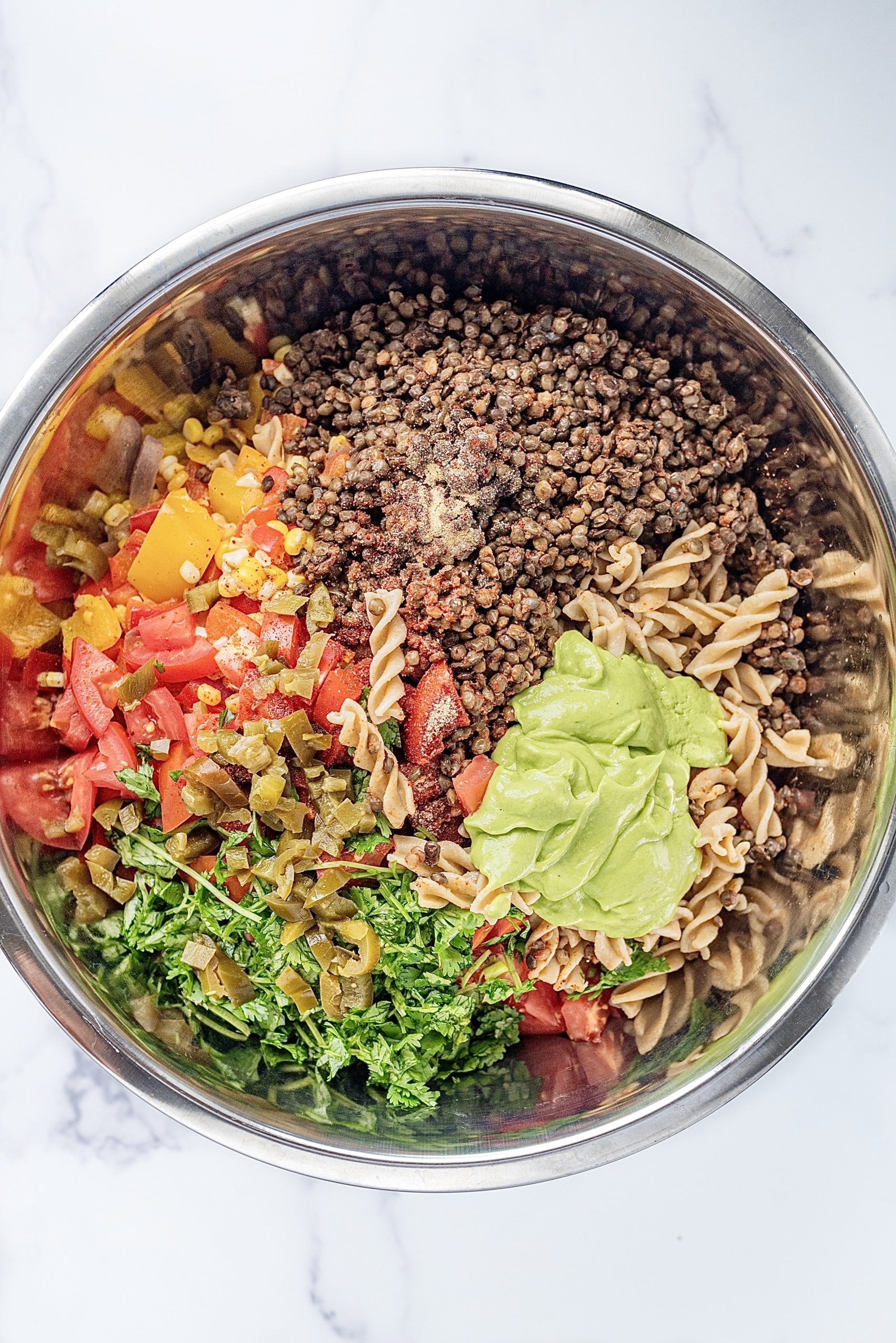 A metal bowl with pasta, lentils, sauteed peppers, onions, and corn, and fresh cilantro.