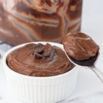 A bowl of chocolate pudding topped with chocolate chips and a spoon with a bite of pudding on it.