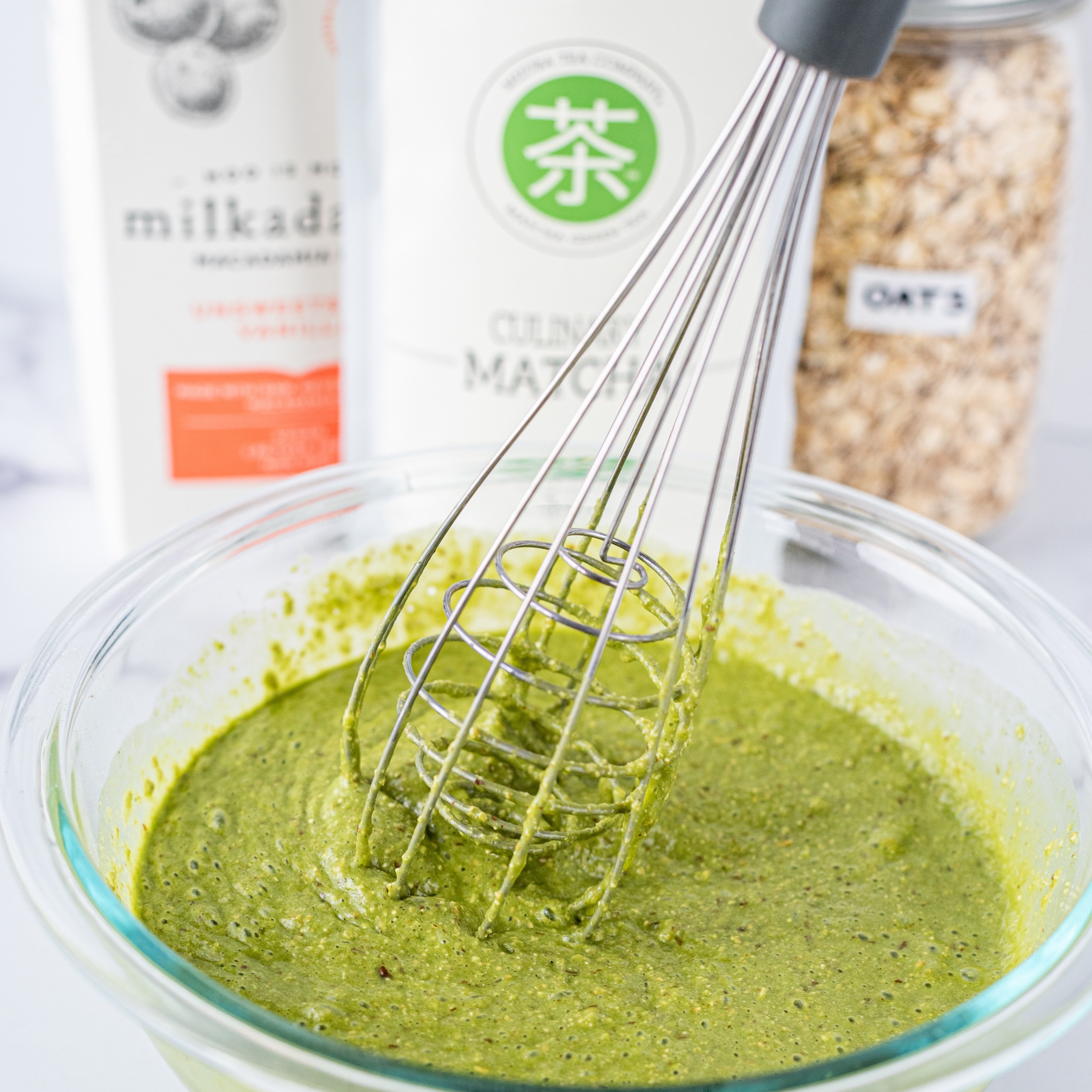 A glass bowl filled with green batter and a whisk in it.