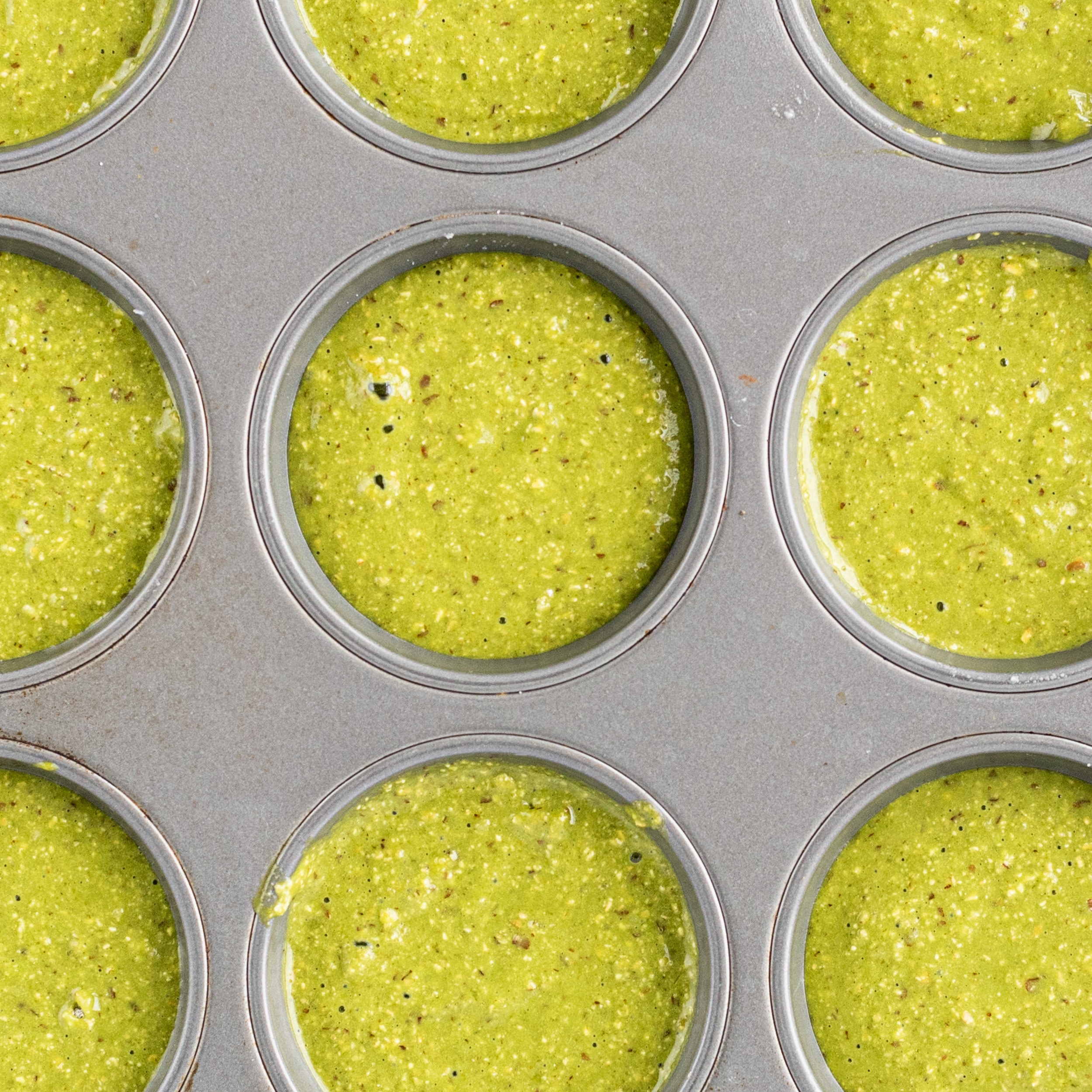 A muffin tin filled with green batter.