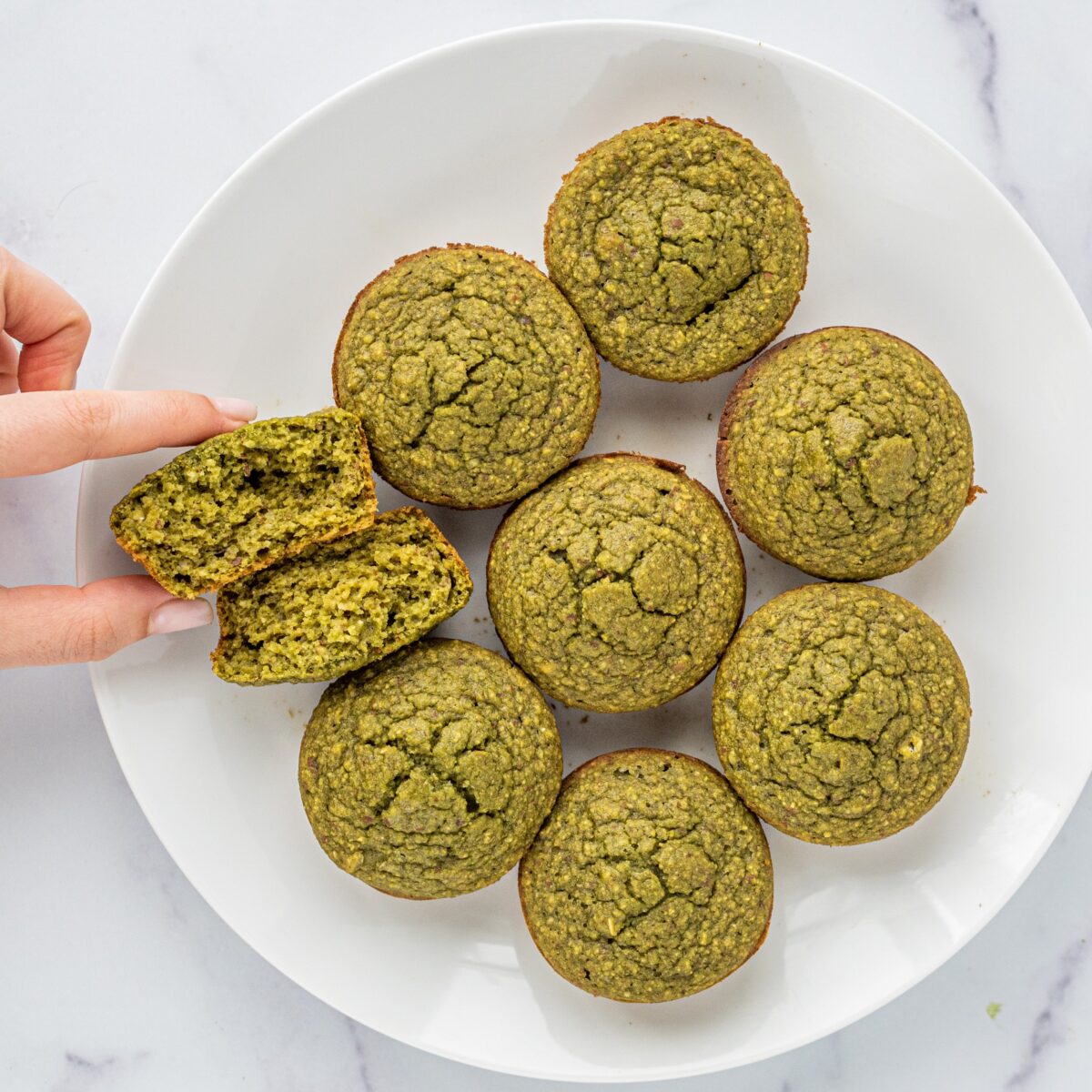 A white plate of 8 matcha muffins with one ripped in half.