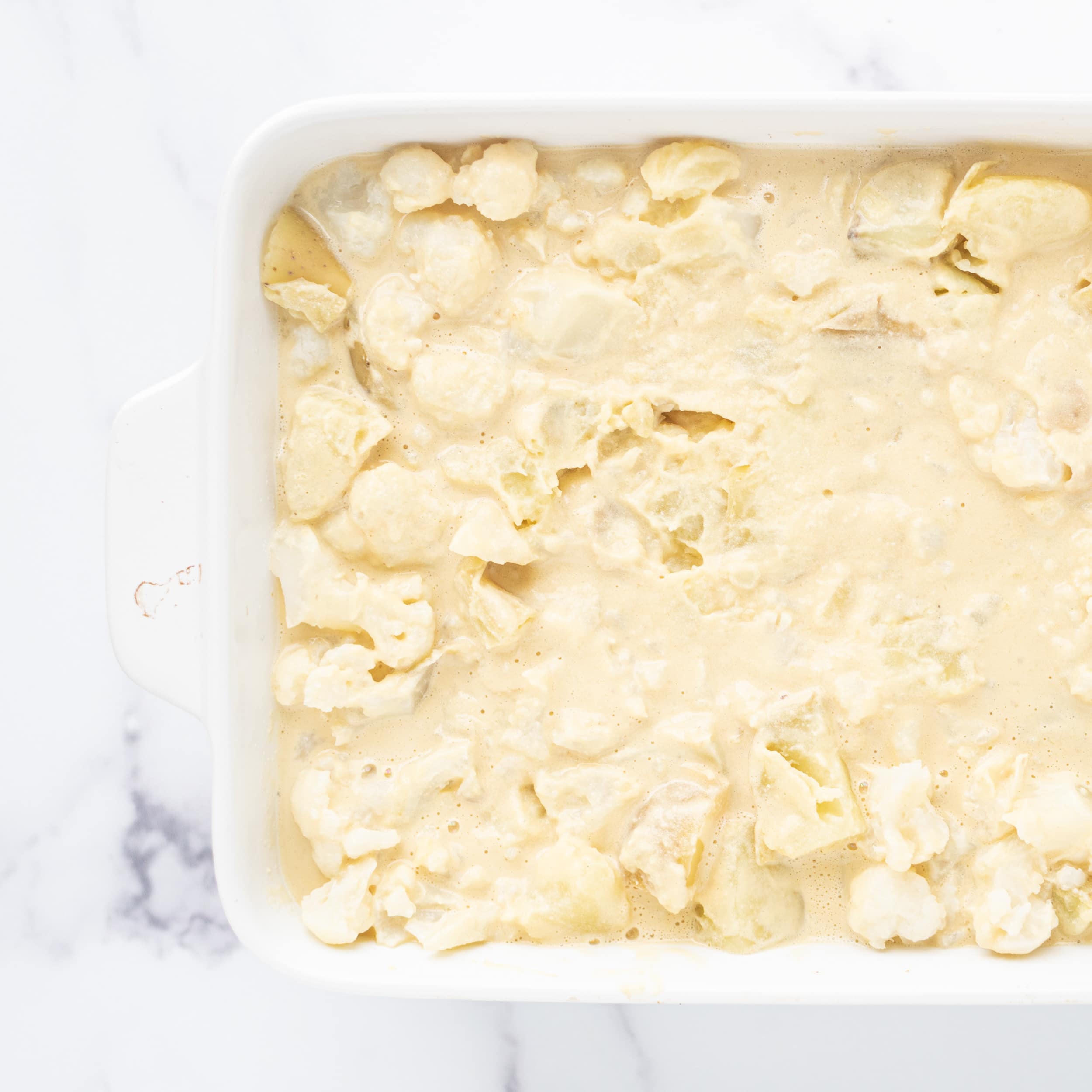 A casserole dish filled with a potato, cauliflower, and cheese sauce mixture.