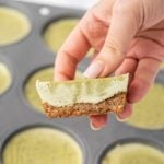 A white hand holding a mini matcha cheesecake cut in half.