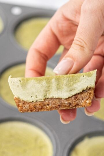 A white hand holding a mini matcha cheesecake cut in half.