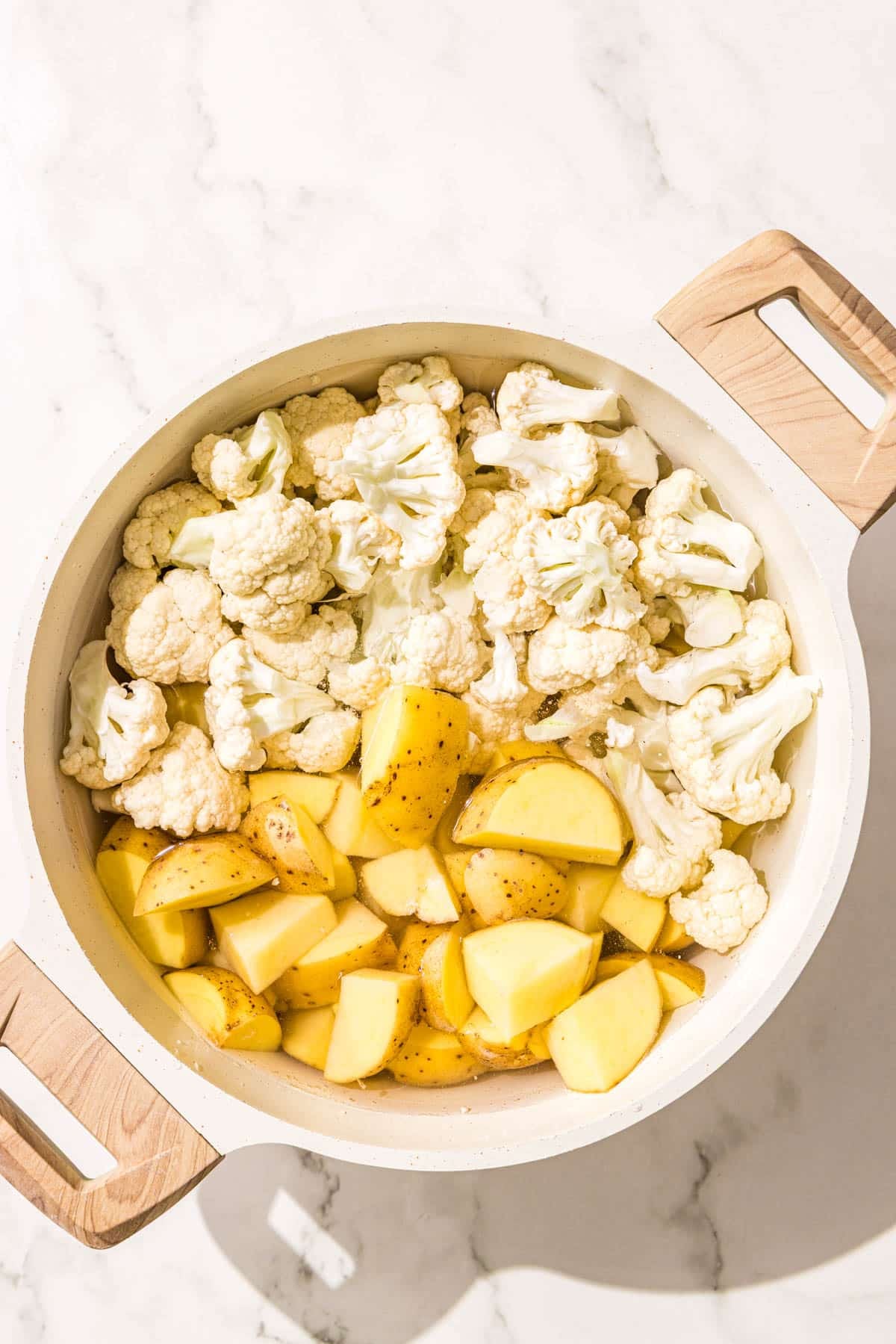 A large white pot with half cauliflower and half potatoes in it.