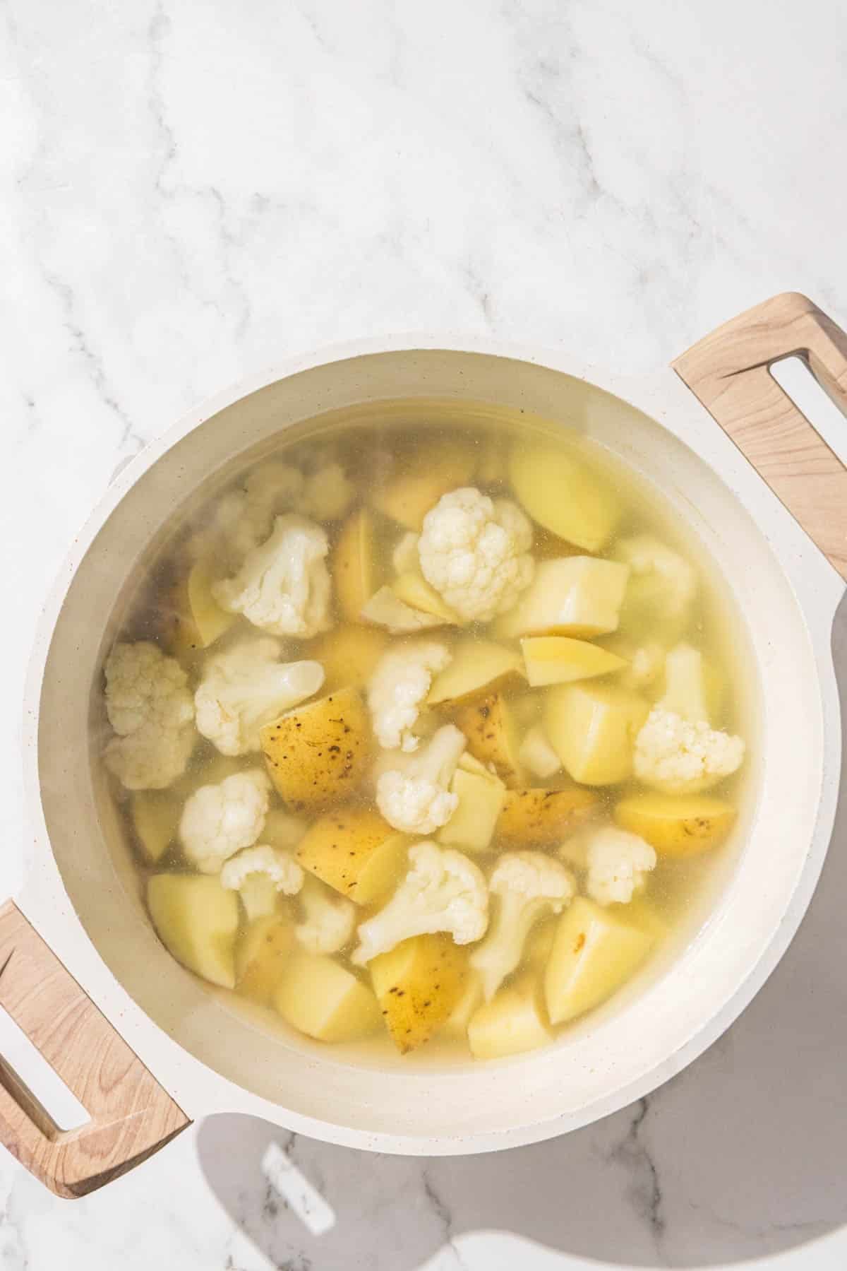 A large pot filled with water and chopped potatoes and cauliflower.