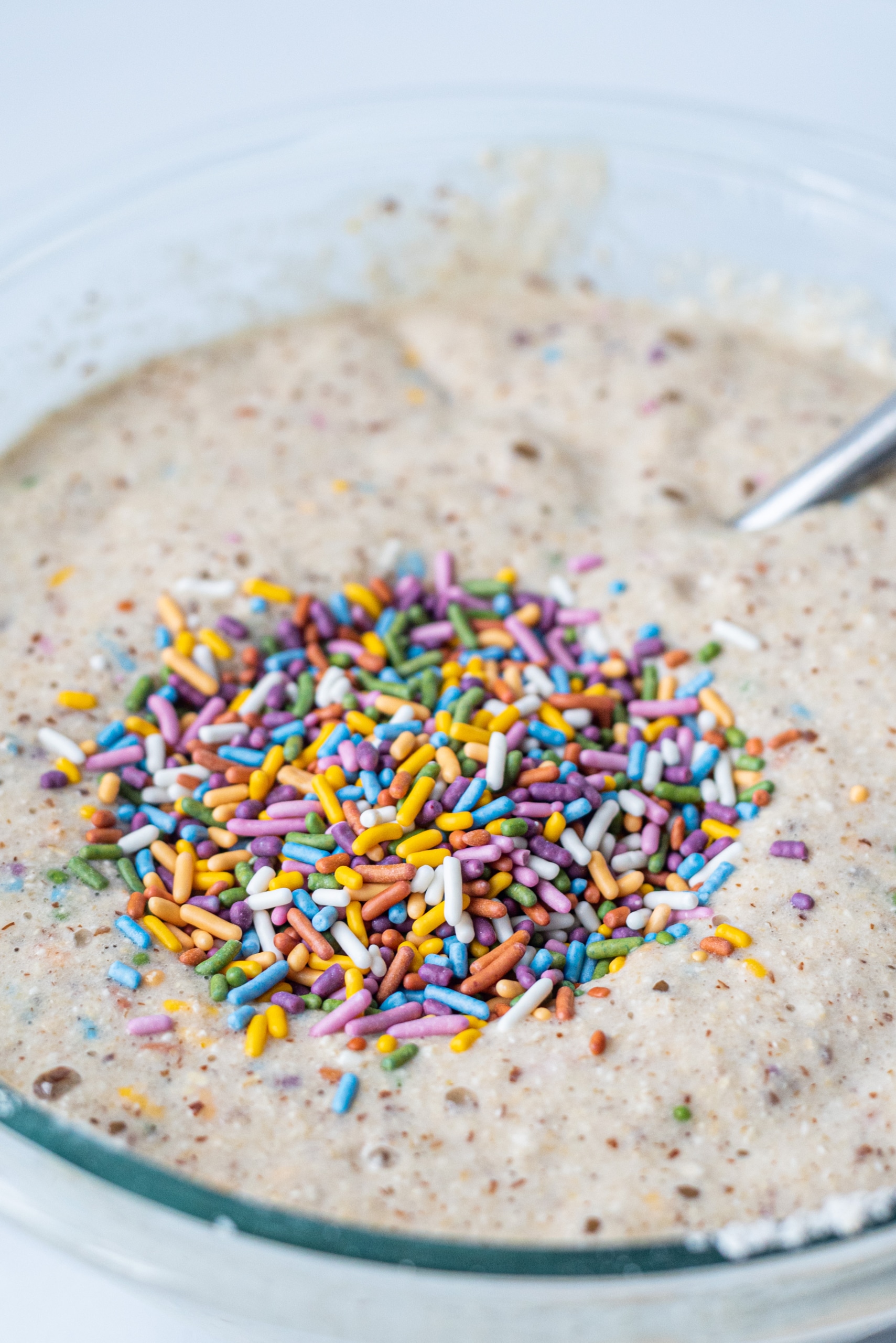 A mixing bowl filled with cupcake batter, sprinkles, and a spoon.