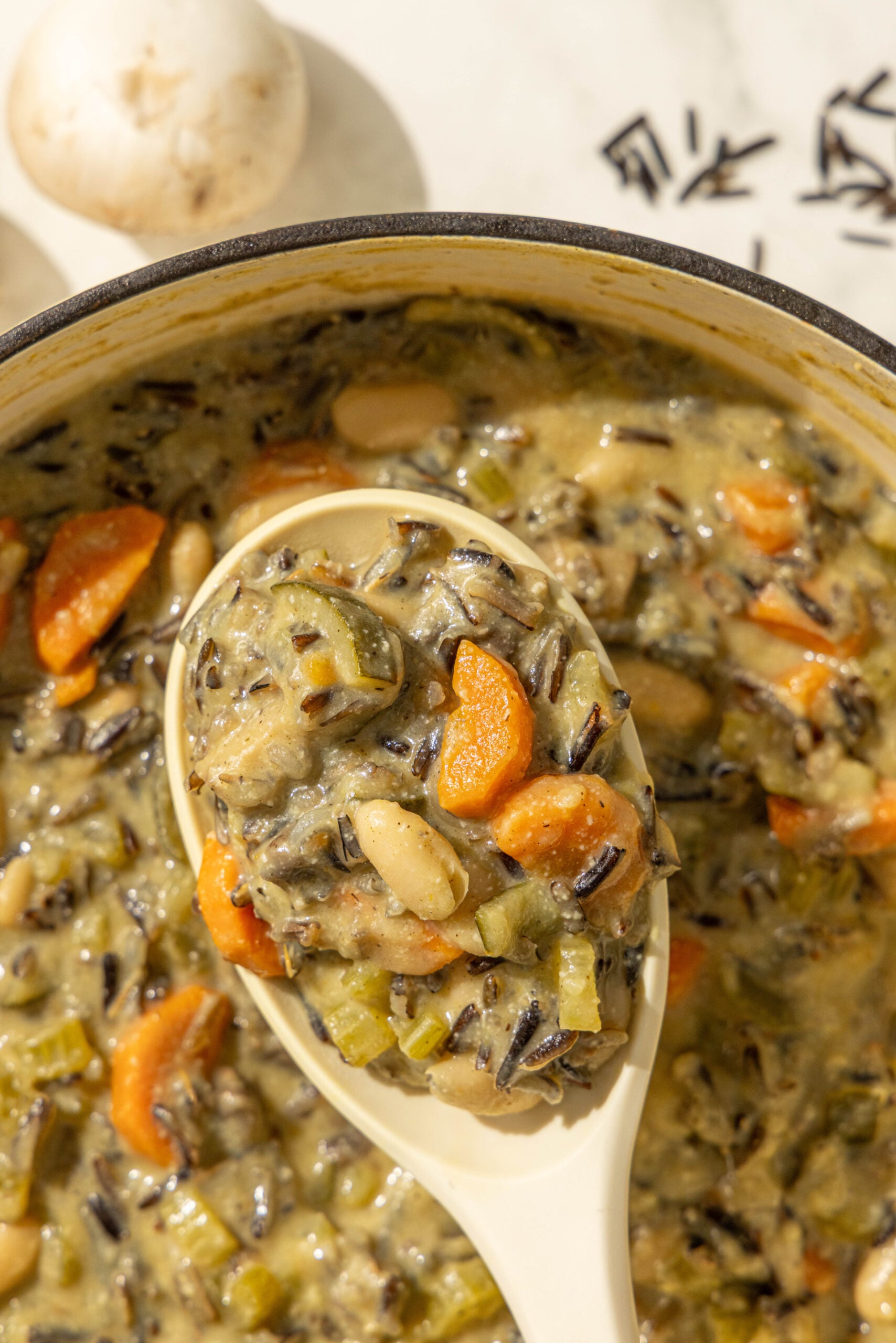 A pot of creamy vegan wild rice soup with a spoon holding a large scoop of the soup.