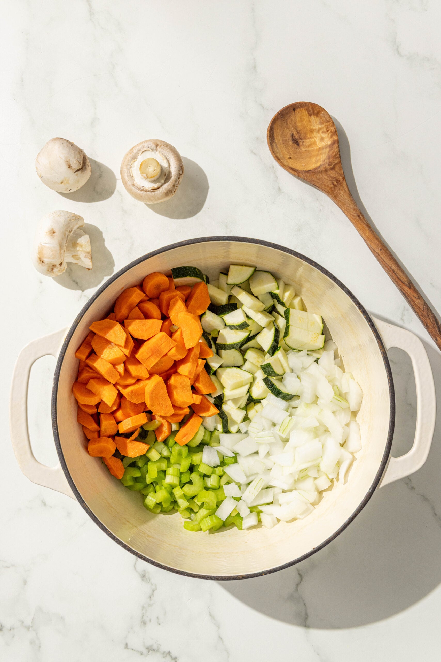 A large soup pot filled with diced onion, celery, carrots, and zucchini.