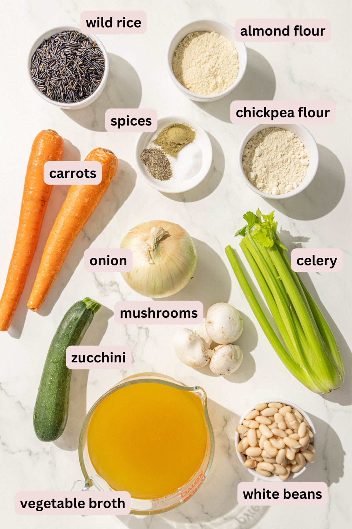 Ingredients laid out on the counter in bowls and labeled including: wild rice, almond flour, chickpea flour, spices, carrots, celery, onion, zucchini, mushrooms, white beans, and vegetable broth.