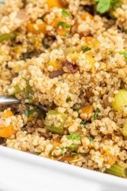 A casserole dish filled with a quinoa butternut squash dish and a silver spoon sticking out.