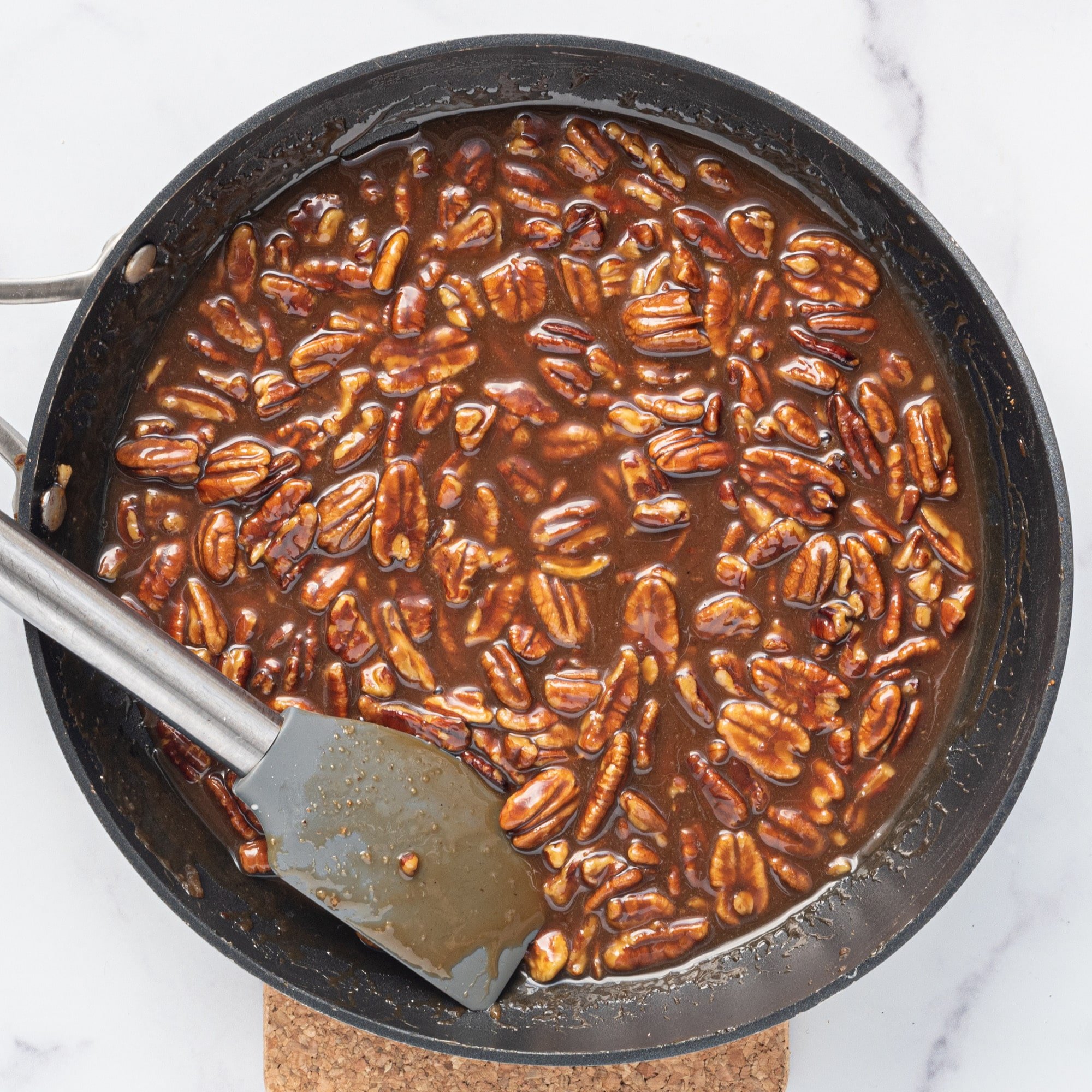 A pot filled with a syrupy pecan mixture and a spatula.