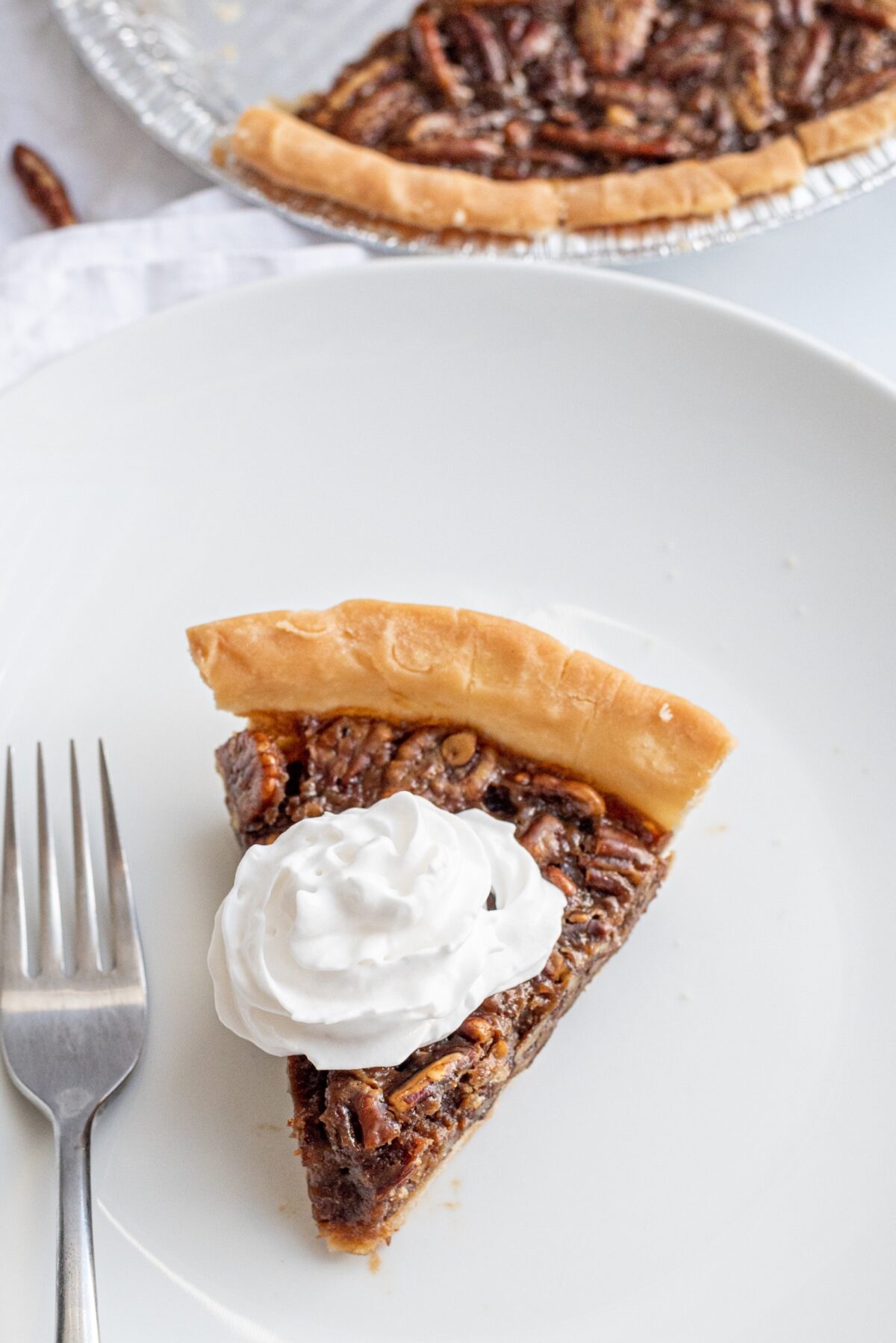 A piece of pecan pie on a white plate topped with whipped cream and a fork.