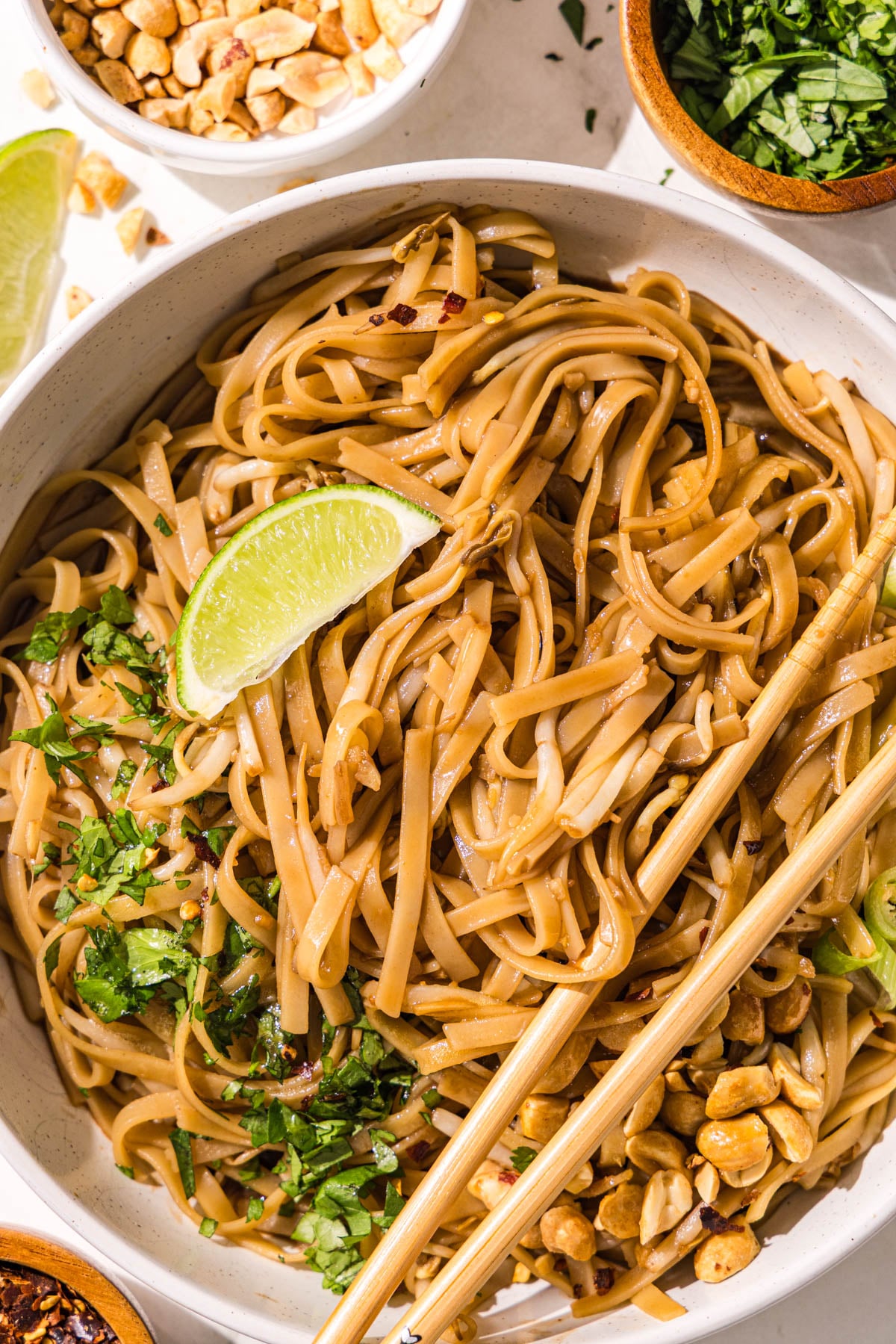 A bowl of vegan pad thai topped with a set of chopsticks, a fresh lime wedge, fresh cilantro, peanuts, and green onion.