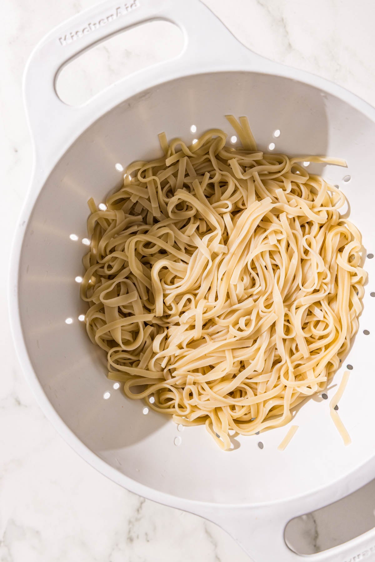 A strainer filled with cooked rice noodles.