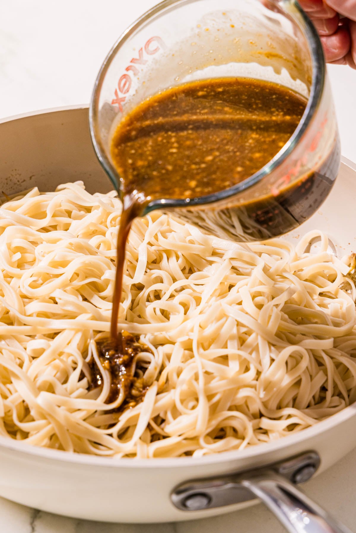 A pan filled with rice noodles and a glass jar filled with sauce poured over the noodles.