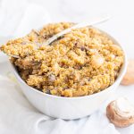 A bowl of Vegan One Pot Mushroom Quinoa Risotto on a white cloth towel with two mushrooms sitting on the counter beside the bowl.